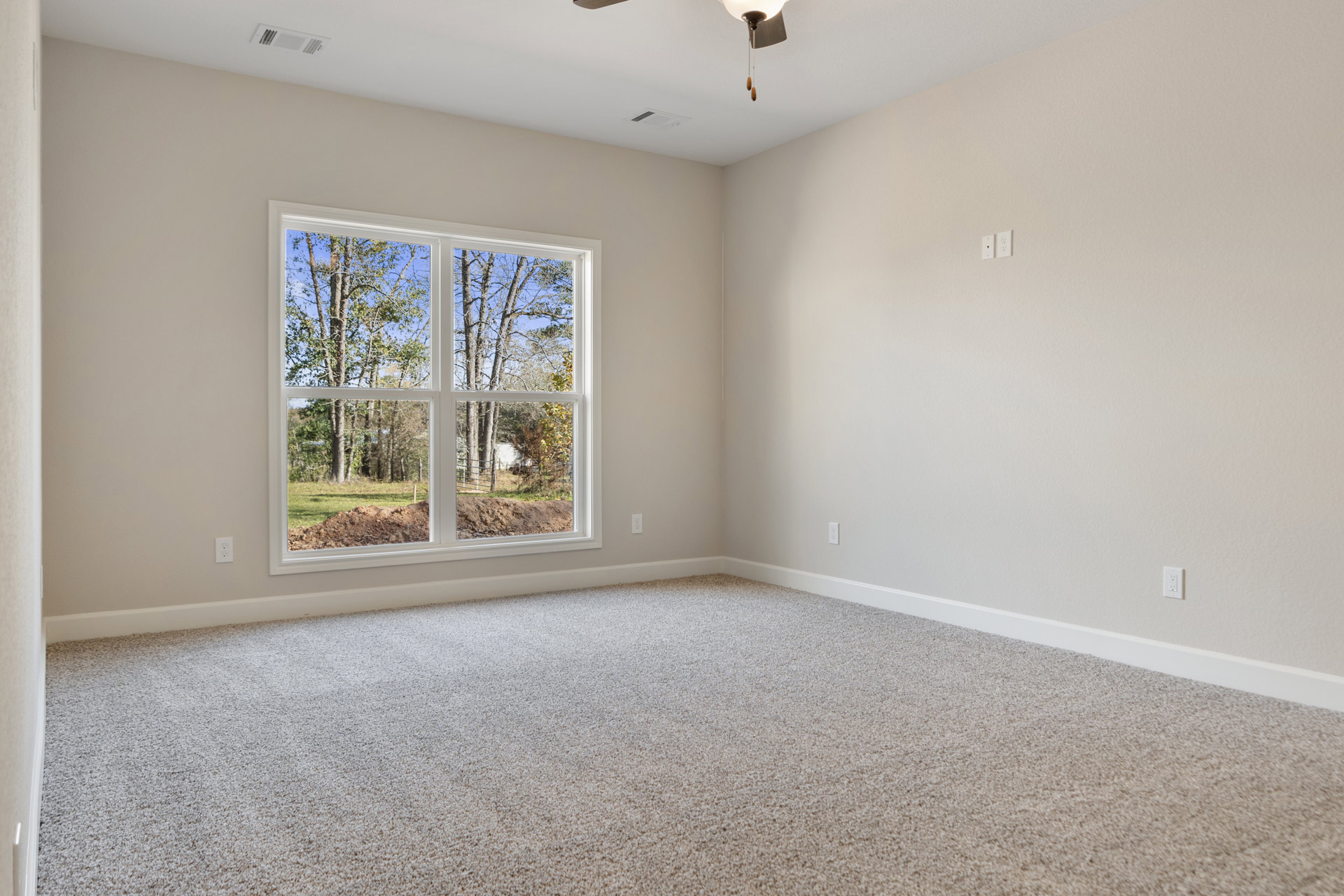 Bedroom with beige carpet flooring, white walls, large window overlooking trees and bare ground, ceiling vent, and simple crown molding.