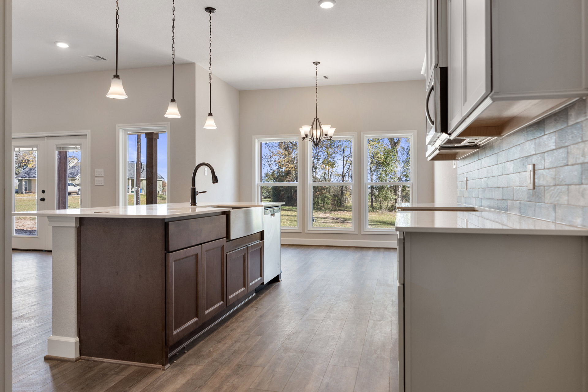Kitchen with wood flooring, white walls, marble-topped island, stainless steel faucet, cabinetry, window, ceiling chain, and pole with sign