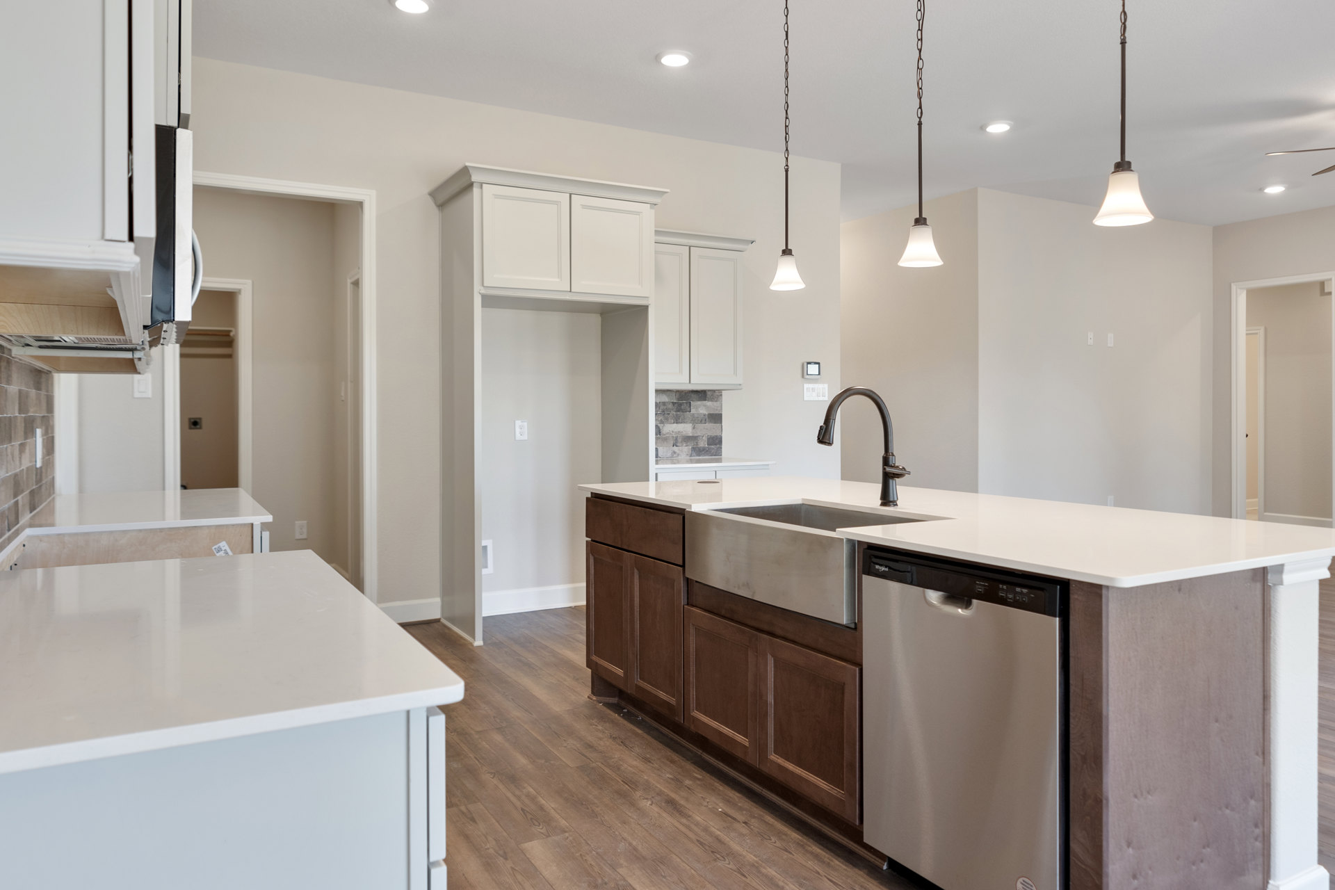 Open kitchen with light wood flooring, white cabinetry, stainless steel dishwasher, black faucet on a white countertop, and modern pendant lighting