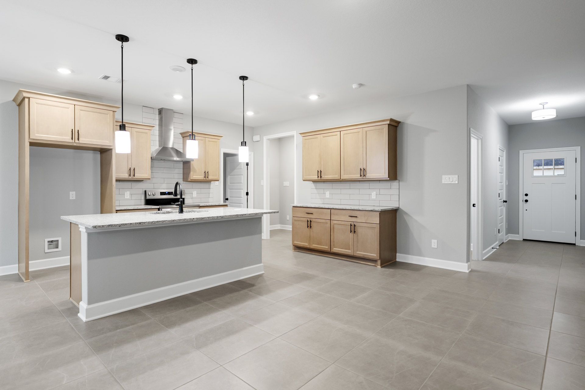 Spacious kitchen featuring a large central island with marble countertop, white cabinetry, black faucet at the sink, and a white door with glass window.