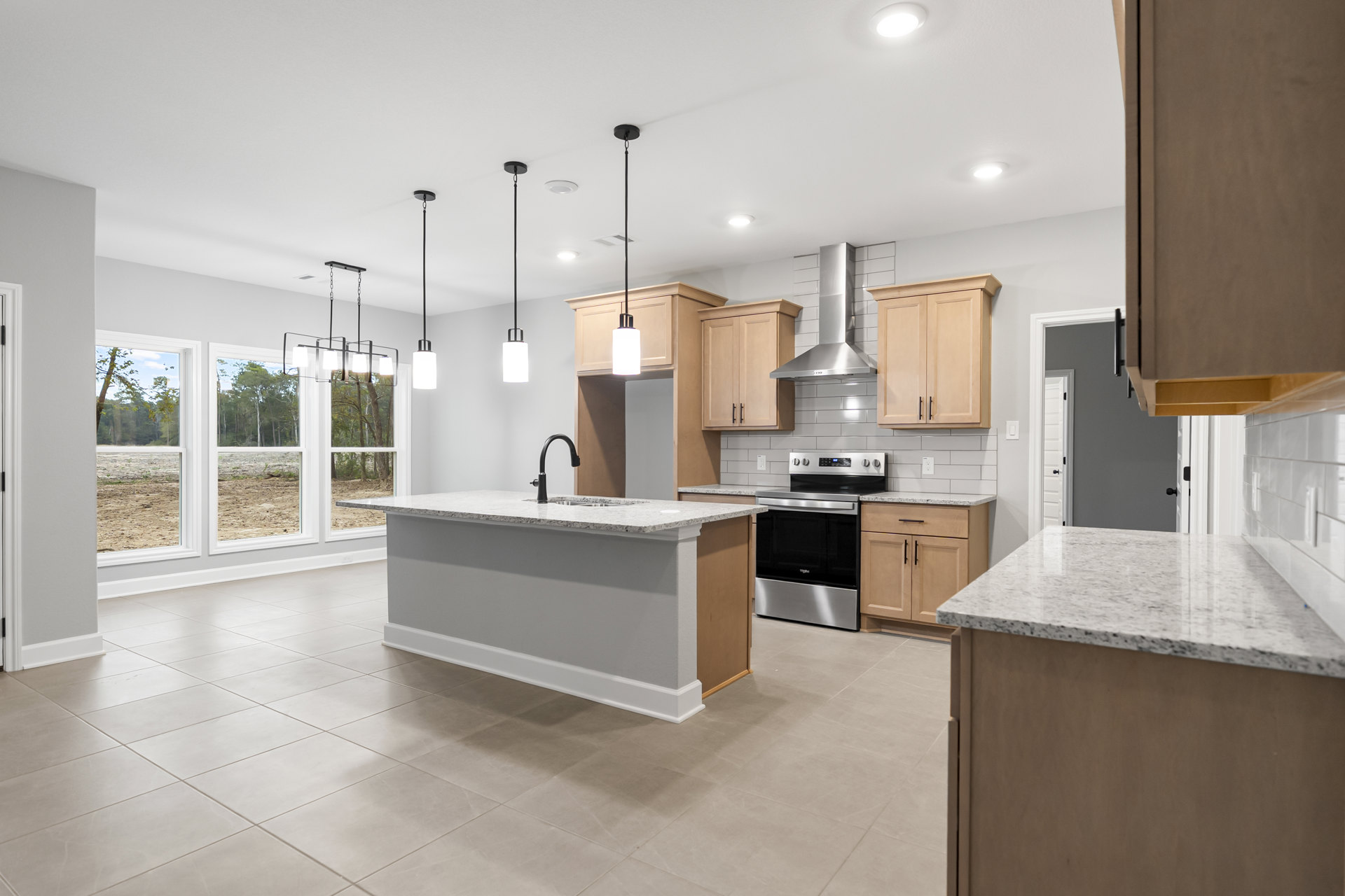 Modern kitchen featuring a central island with built-in sink, stainless steel oven and stove, light wood cabinets with metal handles, stone countertops, and recessed ceiling
