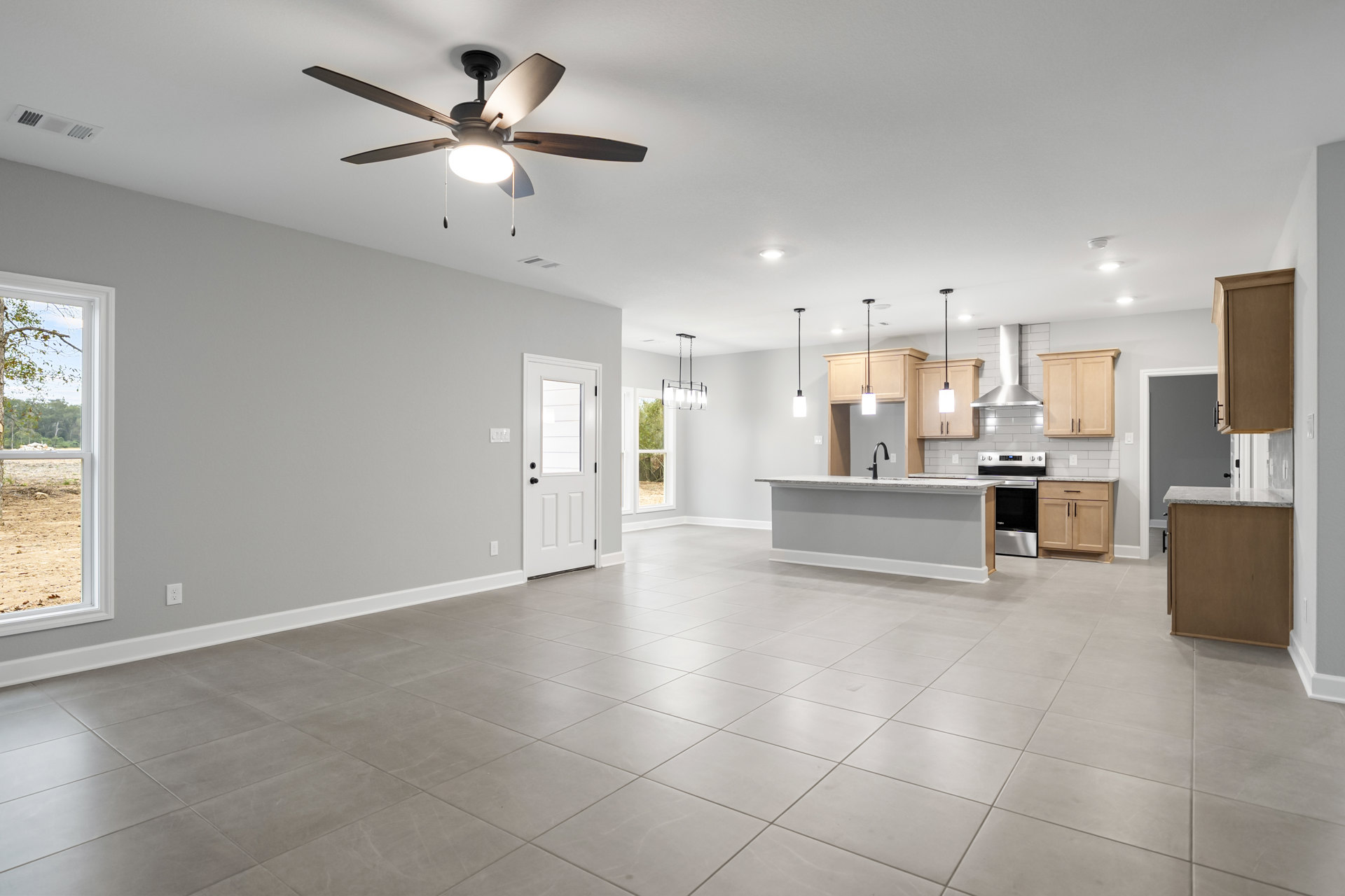 Spacious kitchen and dining area with white tile flooring, ceiling fan with light, white door featuring a window, large window overlooking forest and rocks, close-up of cabinetry.