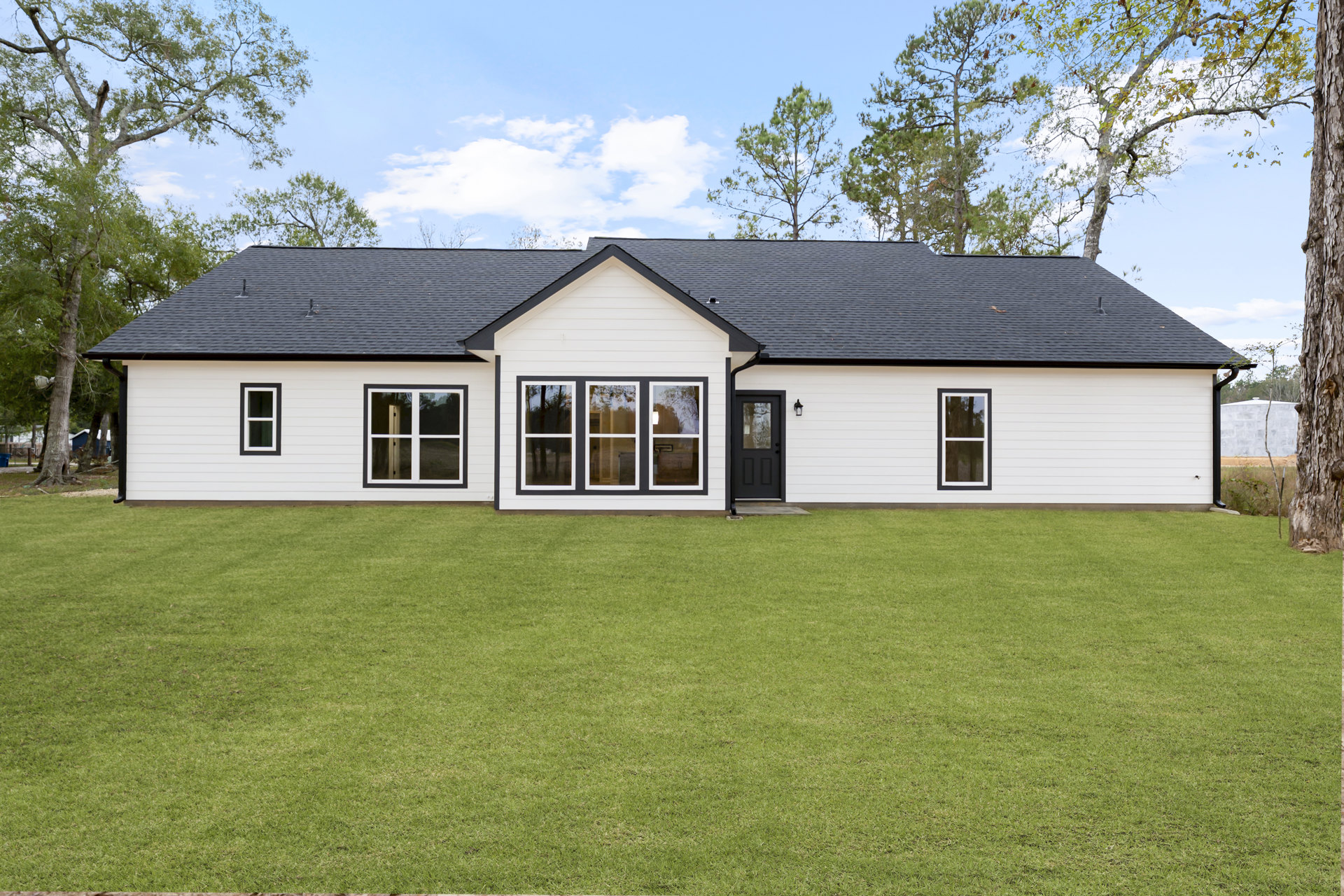 White house with black trim and roof, green lawn in front, white-framed windows, and a central entry door
