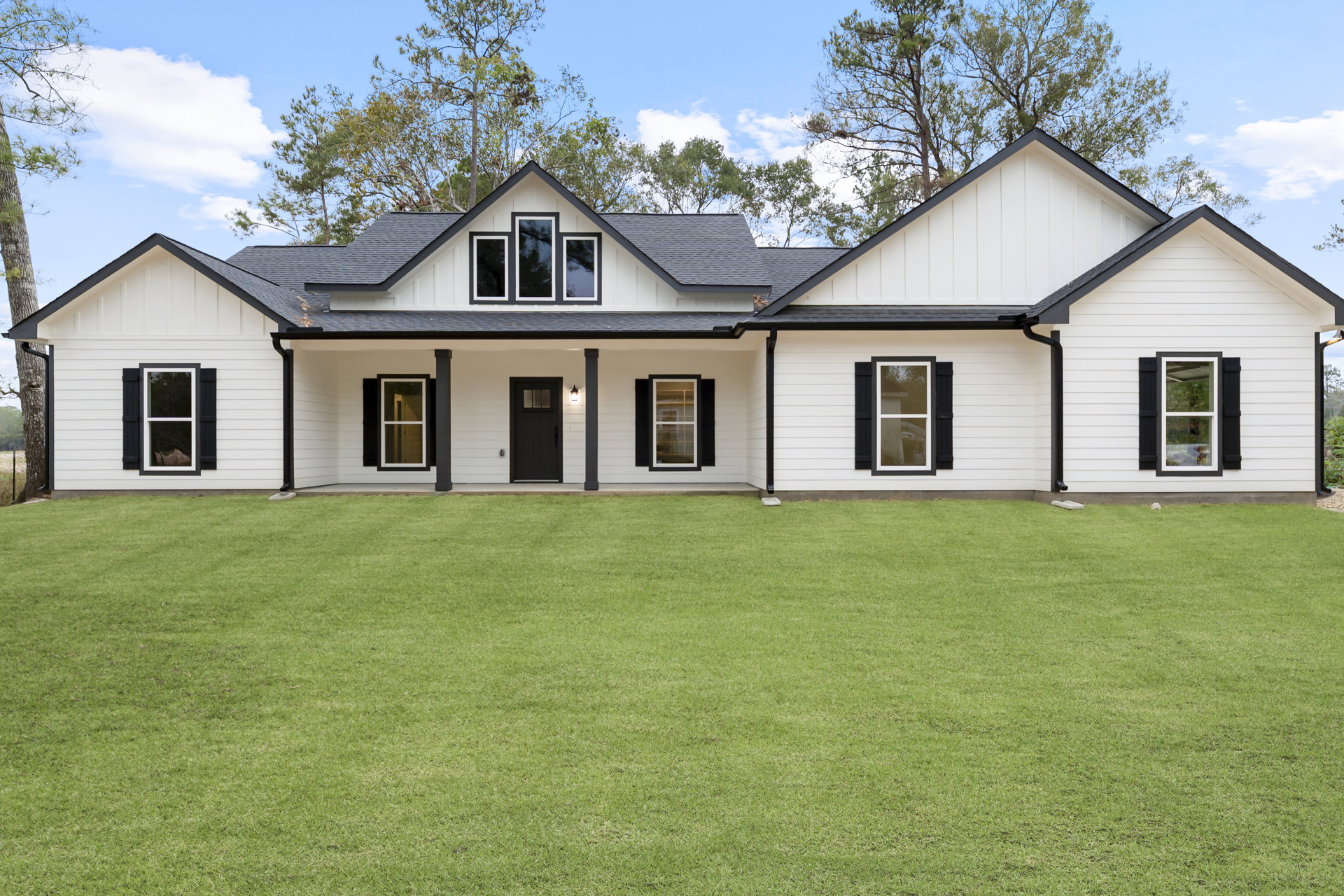 White farmhouse with black door and white-framed windows, surrounded by green lawn under partly cloudy sky, Little White House visible in background