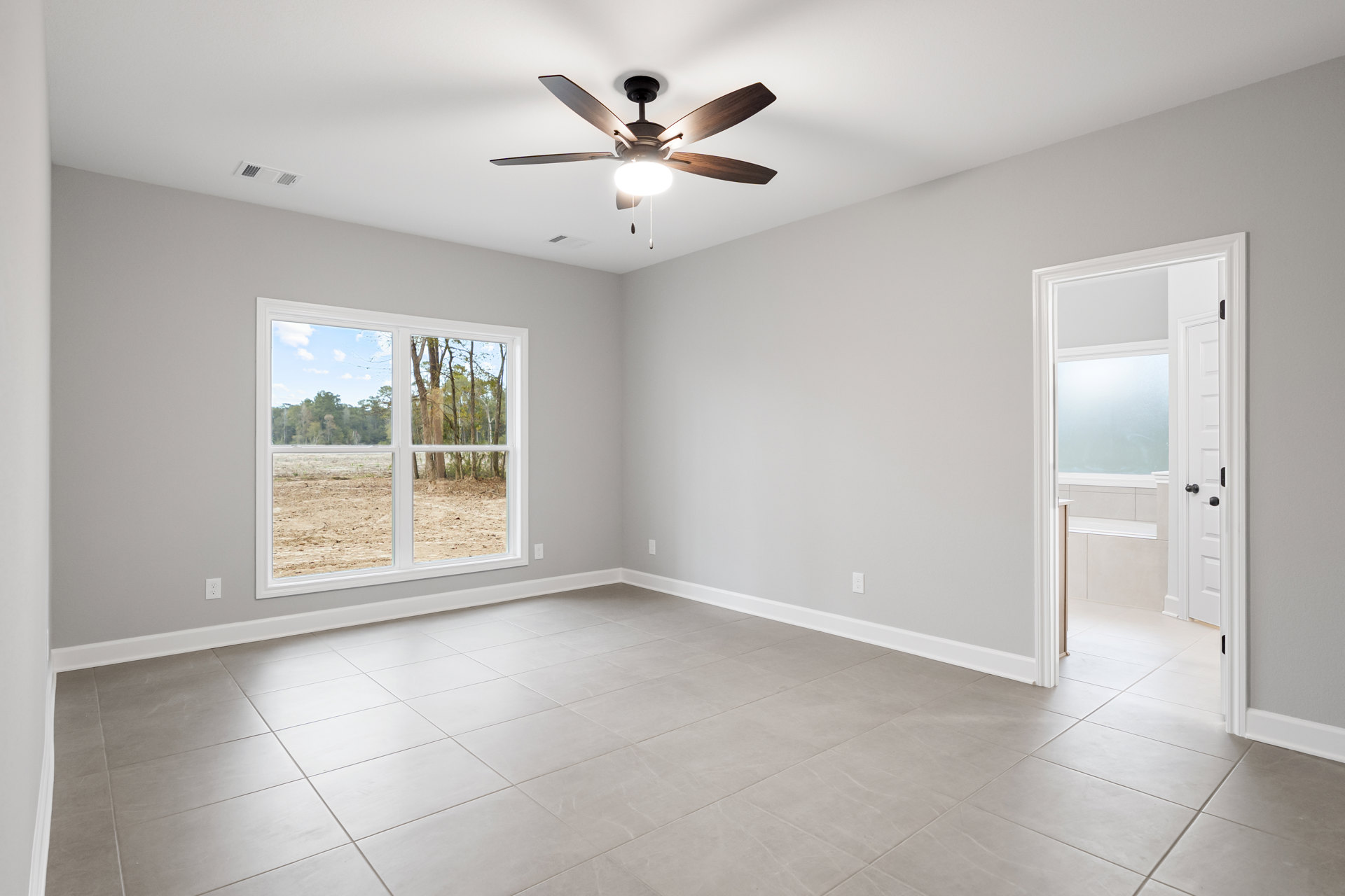 Ceiling fan with light fixture, large window showing trees outside, grey tile flooring, white walls, door with frosted glass panel