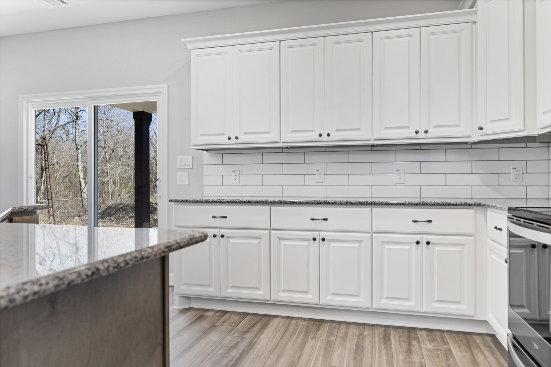 White kitchen with marble countertops, shaker-style cabinets, glass cabinet doors, black hardware, and square panel white door