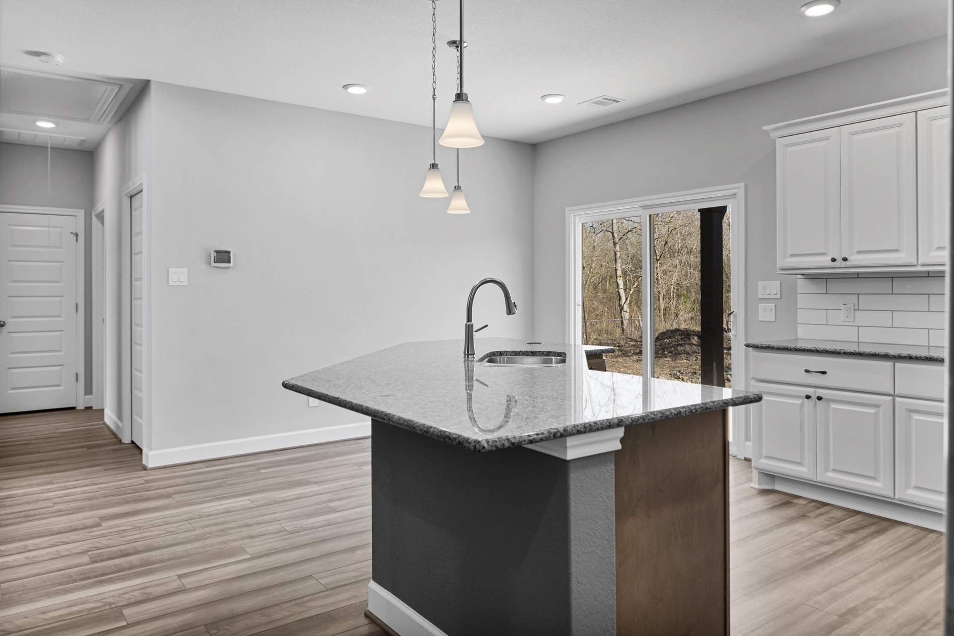 Kitchen with wood flooring, white cabinetry, central island featuring a sink and chrome faucet, stone countertops, recessed lighting, and a white door with a silver handle