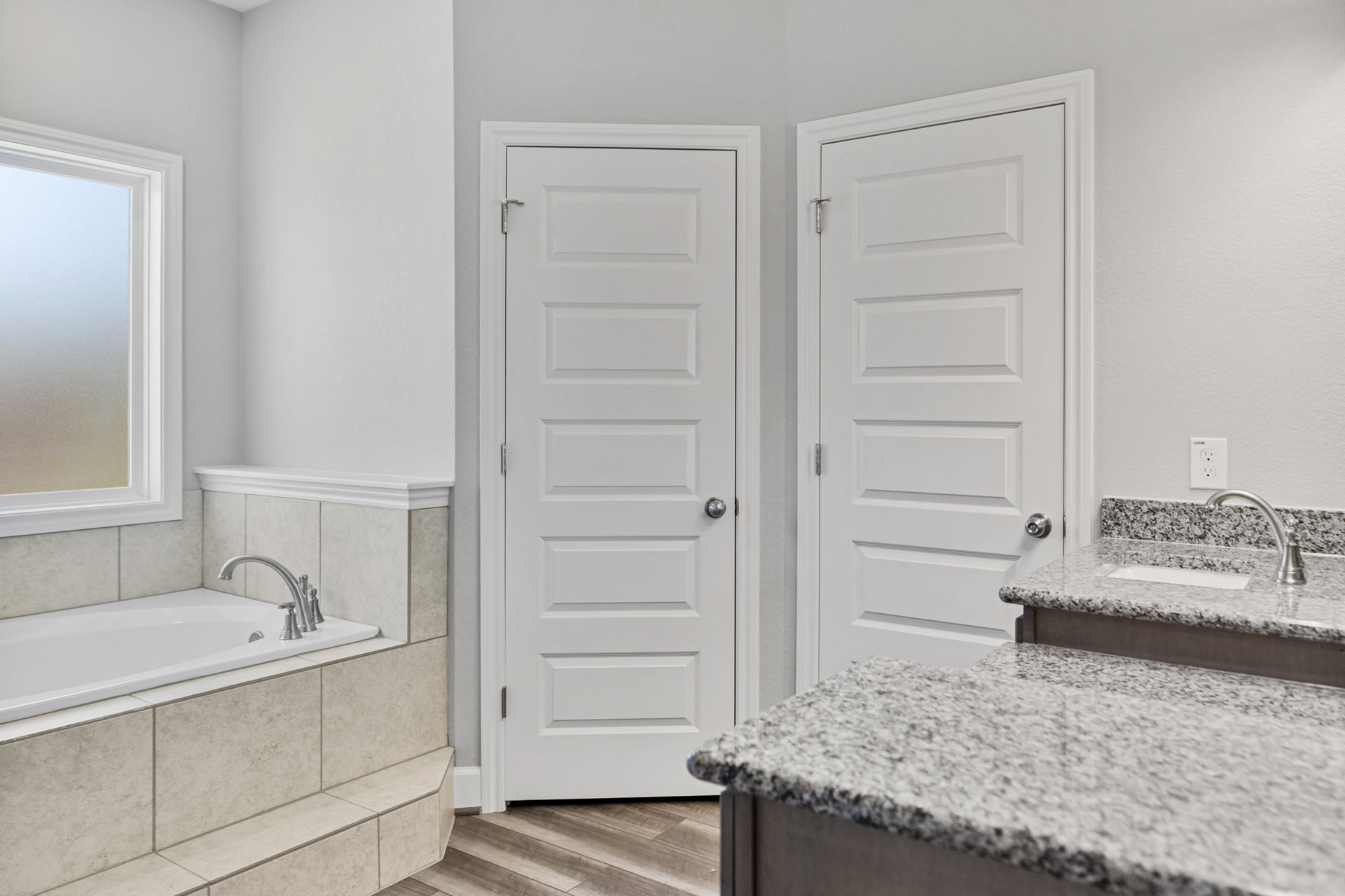 Bathroom with two white doors, freestanding bathtub, tiled floor, light-colored countertop, silver hardware, window, and sink with modern plumbing fixtures