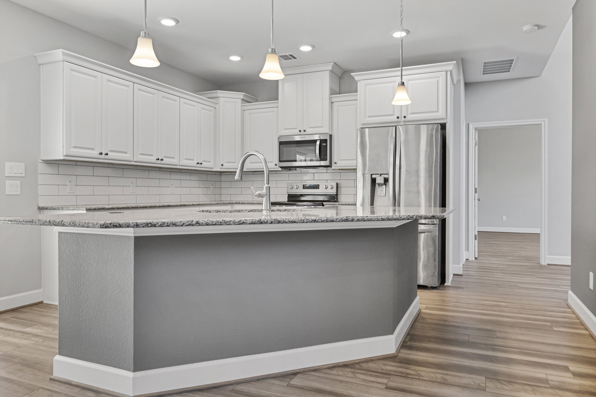 Spacious kitchen featuring a large central island with quartz countertop, white cabinetry, stainless steel microwave, undermount sink with silver faucet, white tile backsplash