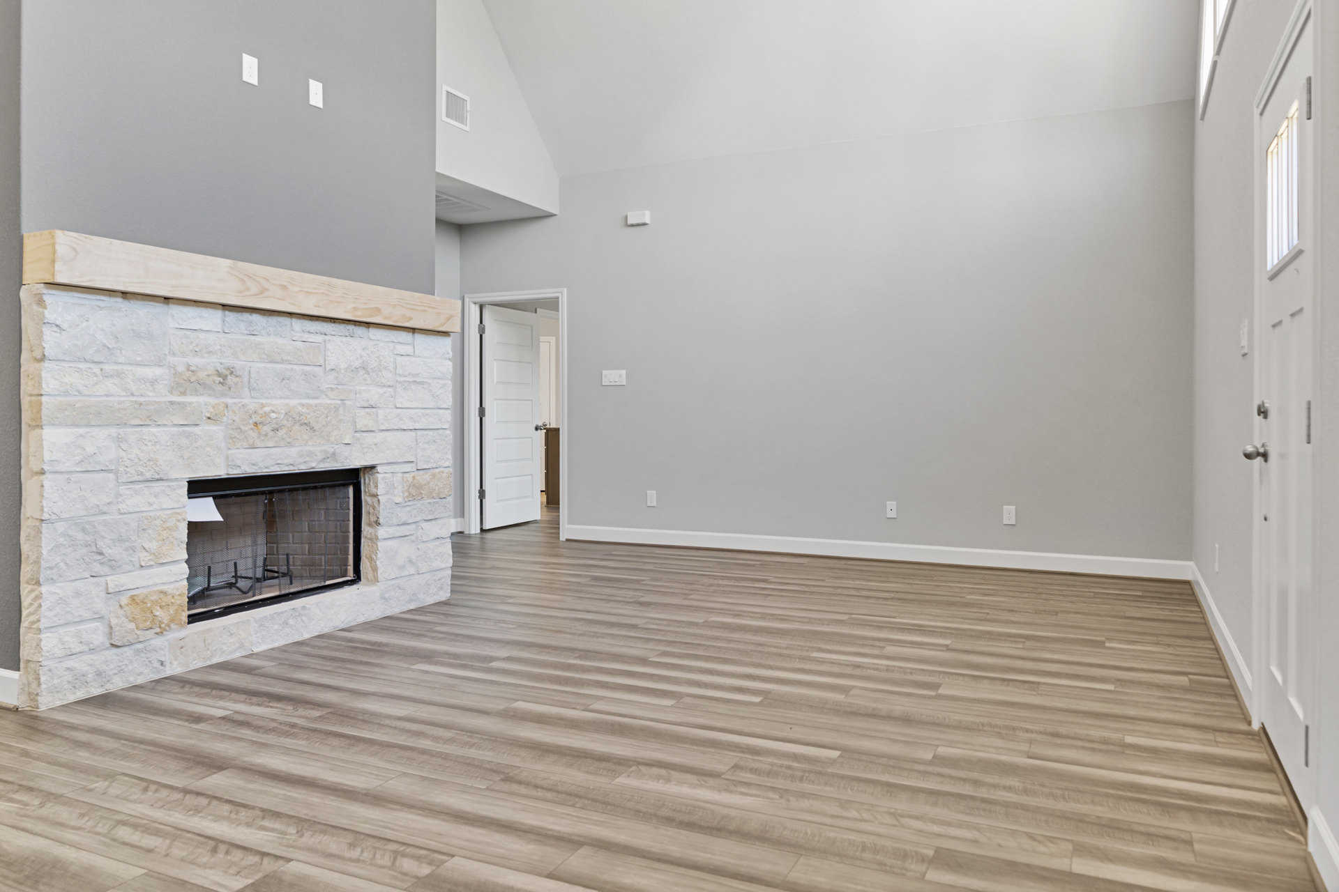 Hardwood flooring and white plaster walls in a living room with a central fireplace, metal screen, and white door with silver hardware