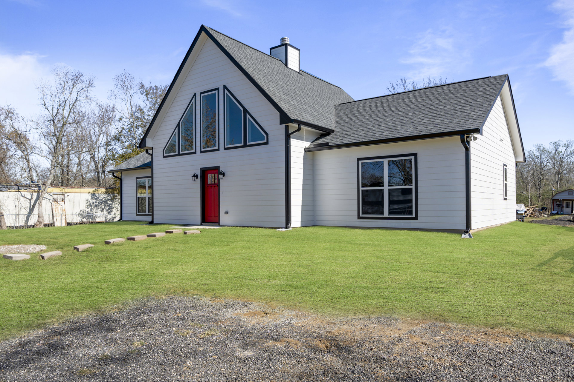 White siding house with red glass-paneled front door, large window reflecting trees, and green lawn under partly cloudy sky