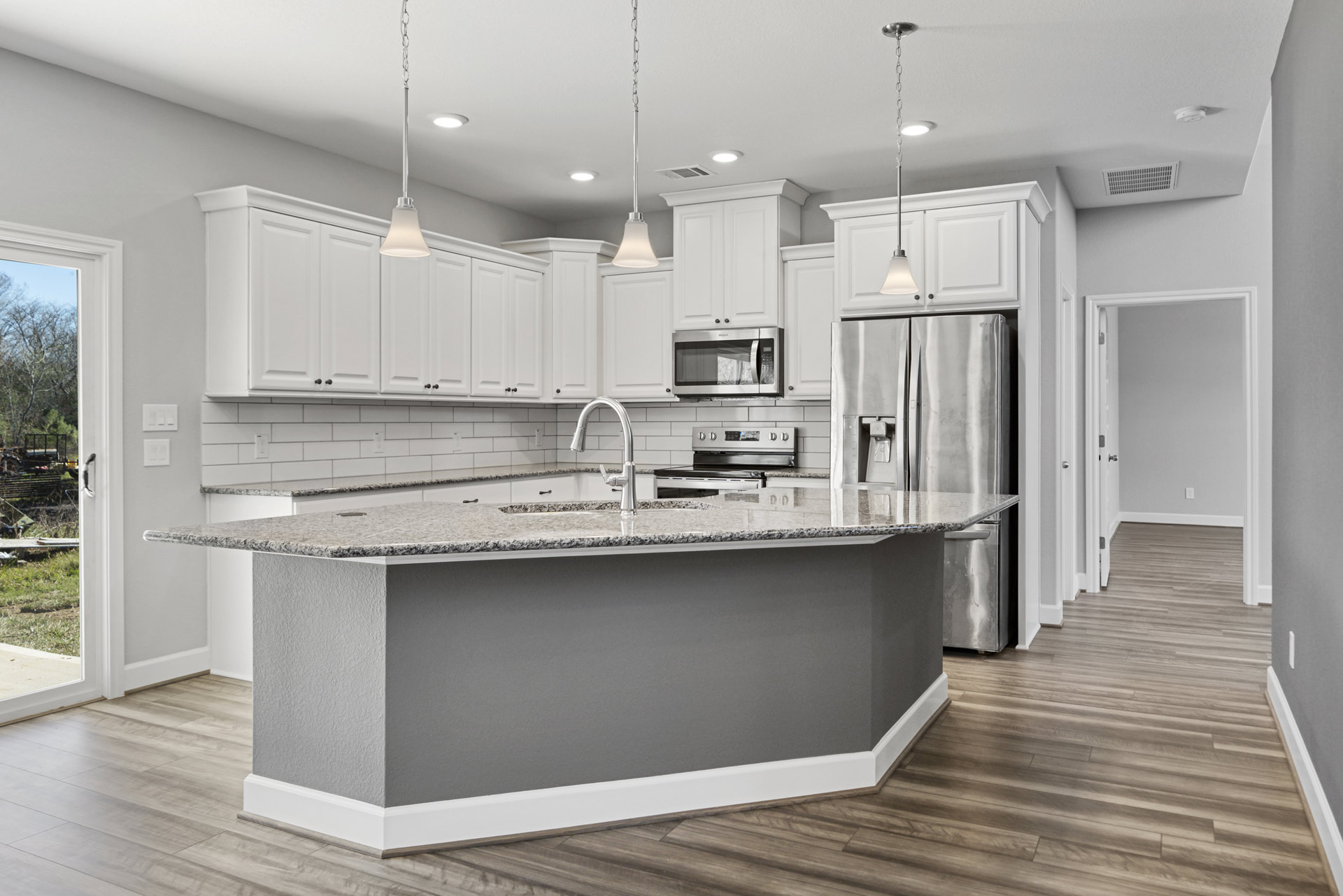 Marble kitchen island with built-in sink and faucet, stainless steel refrigerator, white cabinetry, and microwave, light wood flooring and recessed ceiling lighting
