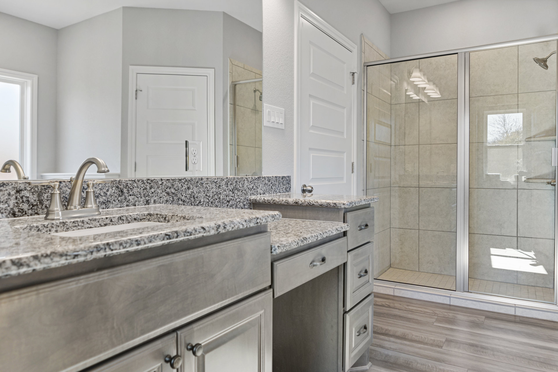 Bathroom featuring a glass shower enclosure, granite countertop vanity with undermount sink, white cabinetry, silver hardware, and tile flooring