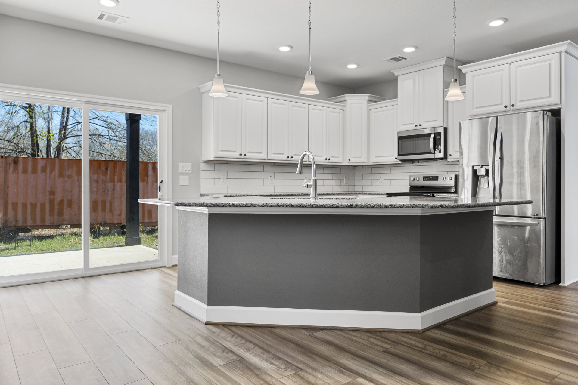 Spacious kitchen featuring a large central island with quartz countertop, open microwave door, undermount sink, stainless steel refrigerator, pendant lighting with chain, white