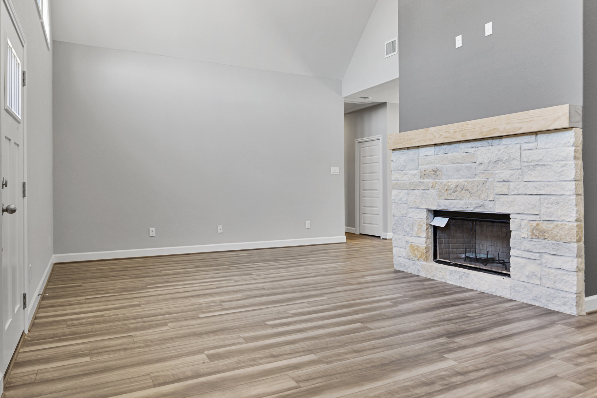 Living room with hardwood flooring, white walls, central fireplace featuring a metal screen, and adjacent white doors.