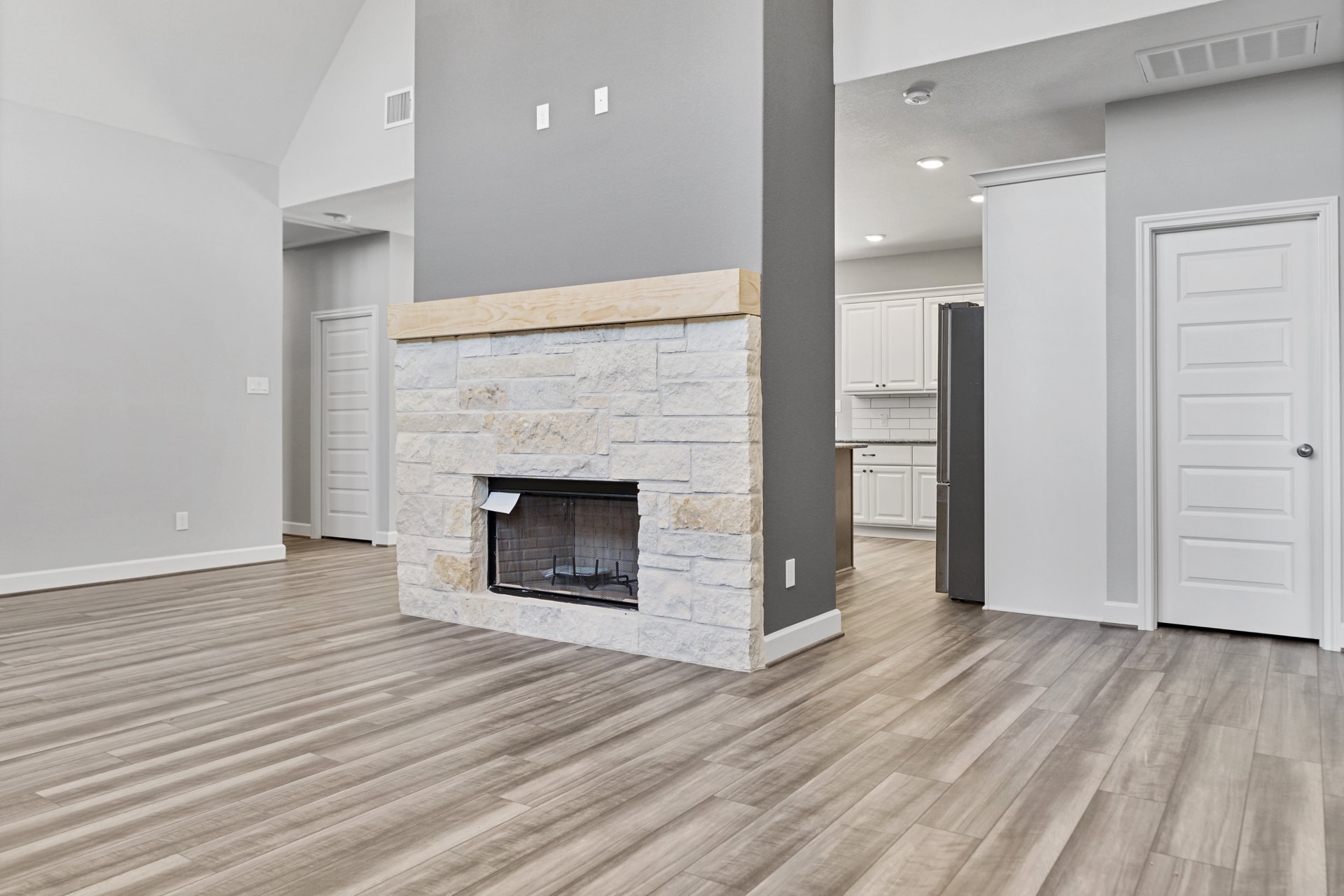 Wood fireplace with dark wood mantle, black metal screen, and attached paper, set against light walls and wood laminate flooring; white door with silver knob visible to the side.