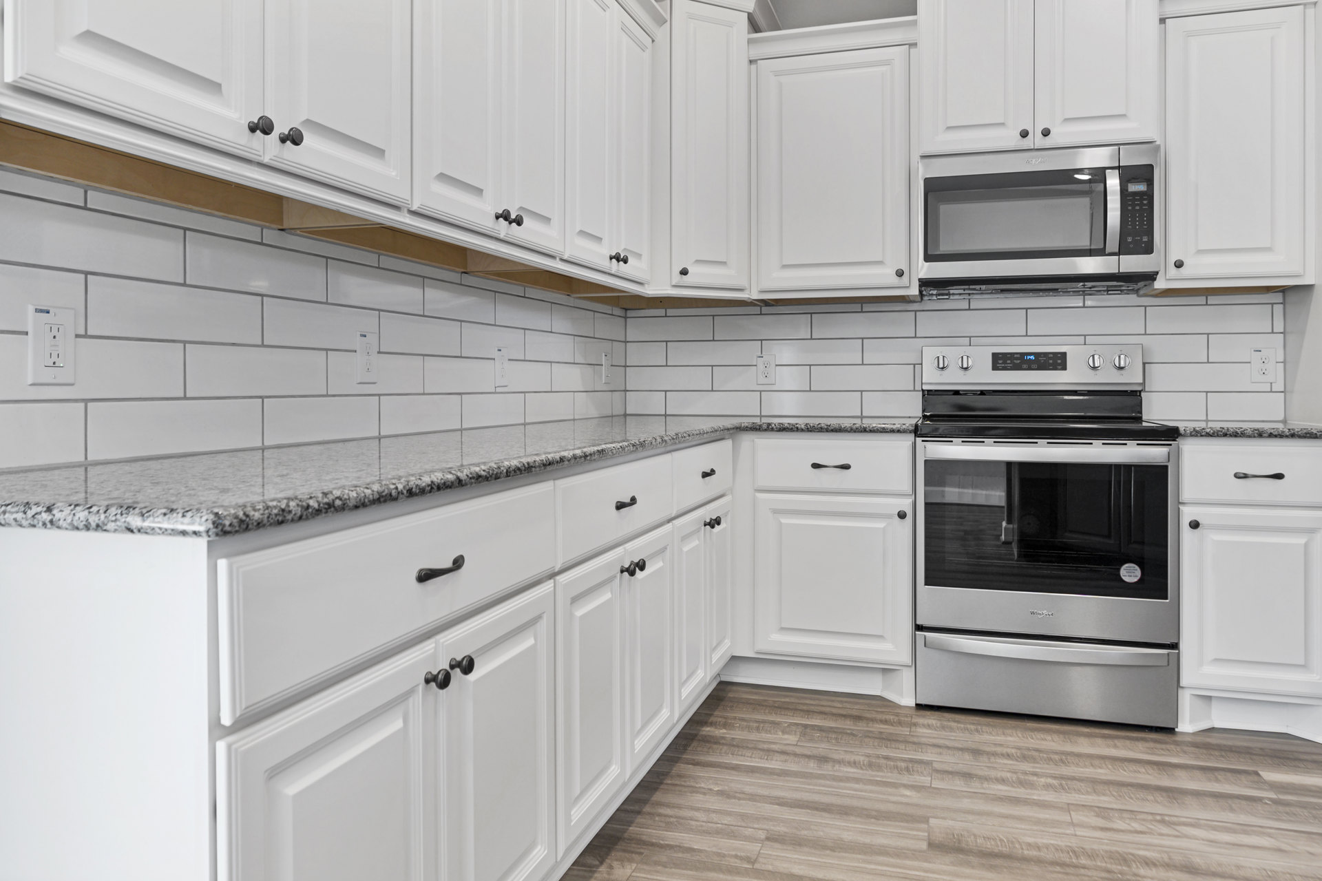 White kitchen cabinets, stainless steel stove with black cooktop, built-in microwave, white door with black handle, wood flooring, silver refrigerator