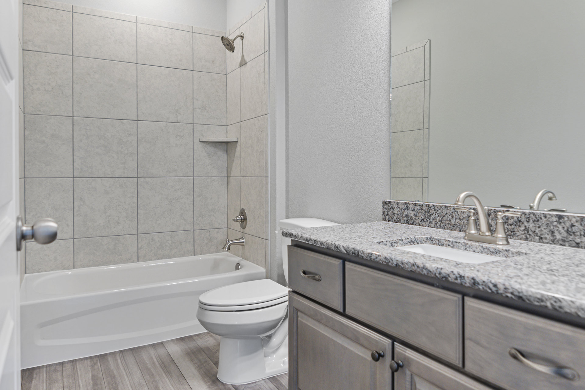 Modern bathroom with white toilet, rectangular sink on stone countertop, wall-mounted faucet beneath large mirror, light gray tile walls, and chrome hardware