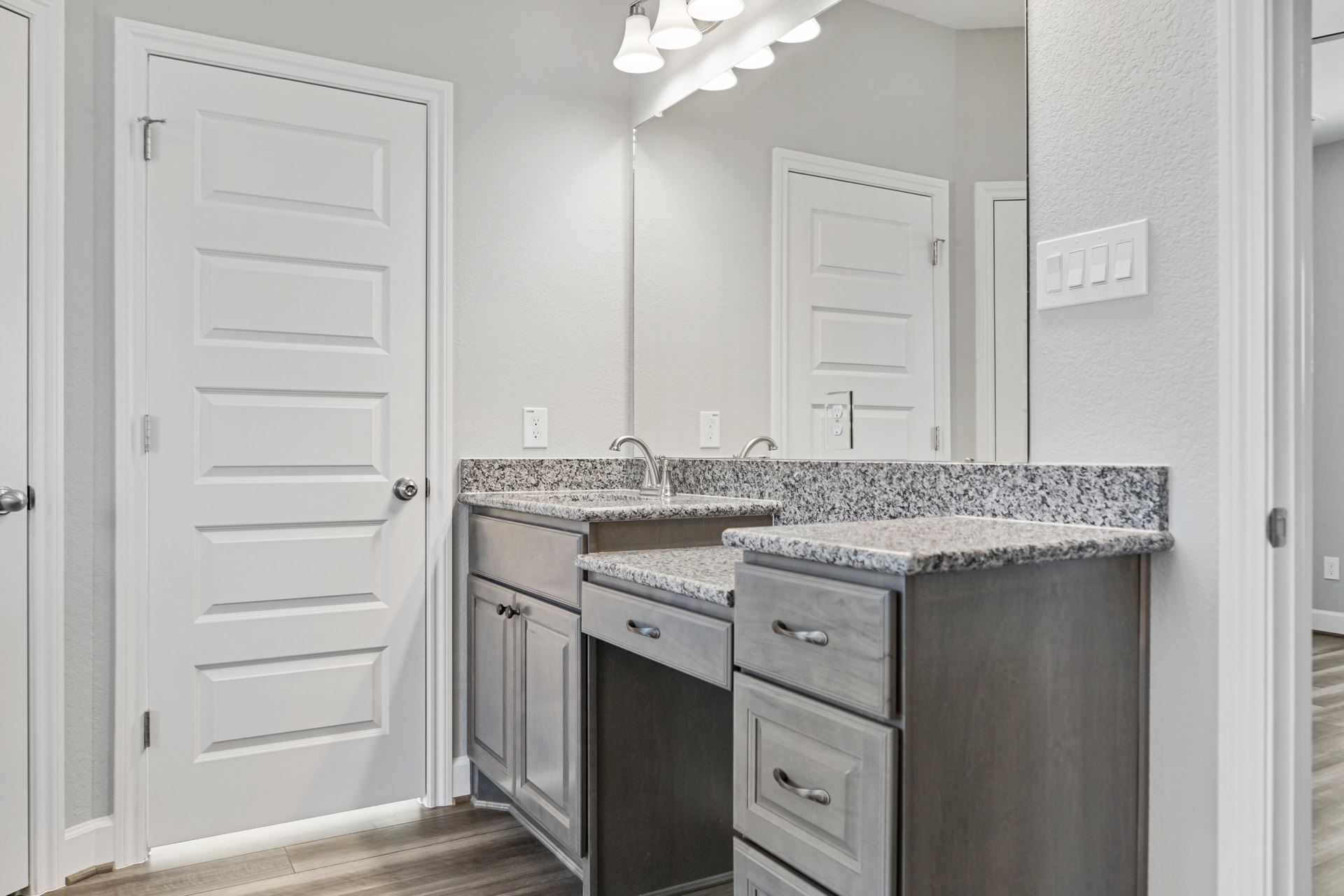 Bathroom featuring marble countertop with built-in drawers, white door with silver handle, rectangular light switch on wall, and cabinetry under sink.