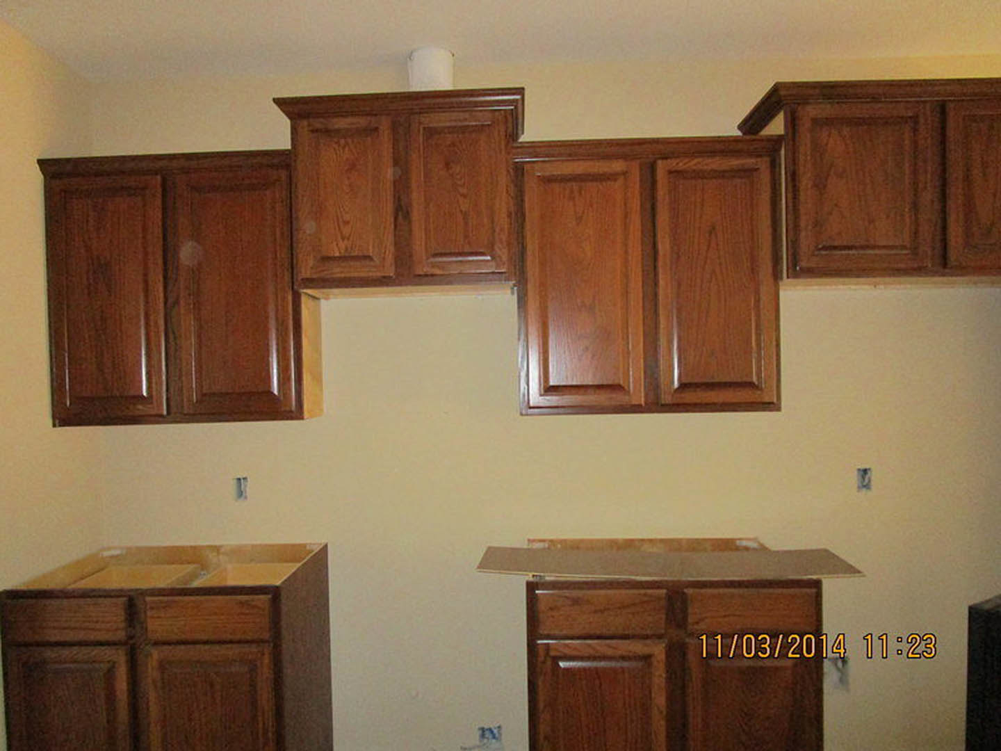 Light wood kitchen cabinets with brushed metal handles, white quartz countertop, built-in stainless steel appliances, and open shelving displaying dishware.