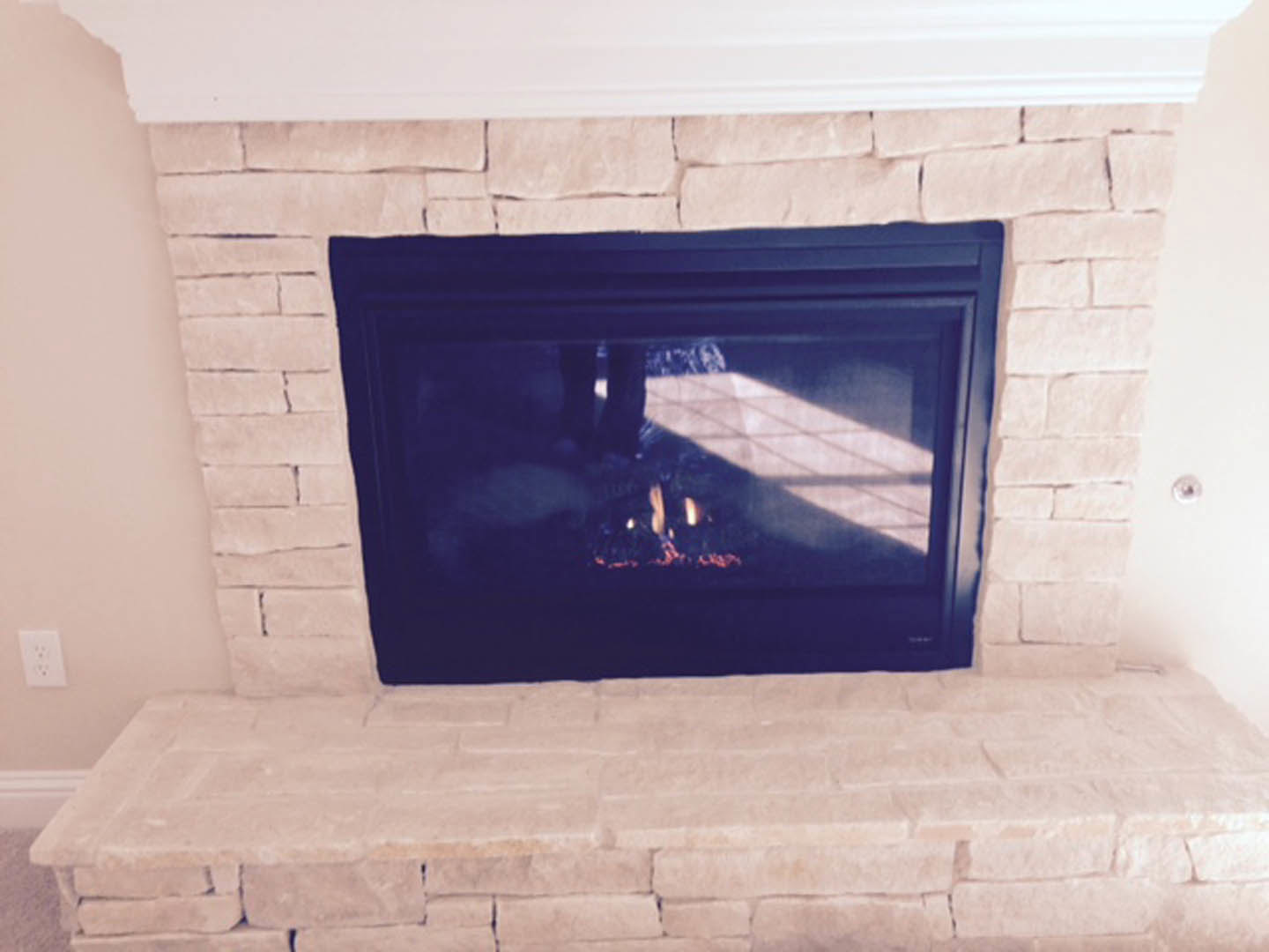 Stone fireplace with glass screen, burning fire, white mantel shelf, and textured stone wall backdrop