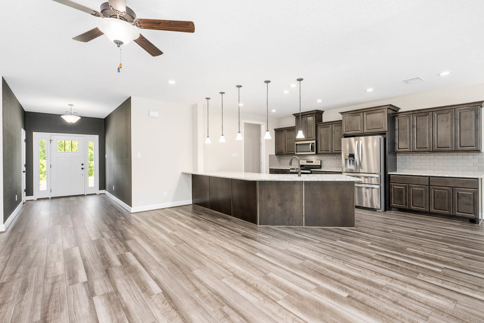 Open kitchen and dining area featuring wood cabinetry, stainless steel refrigerator, granite countertops, ceiling fan with light, white door with glass panes, and large window.