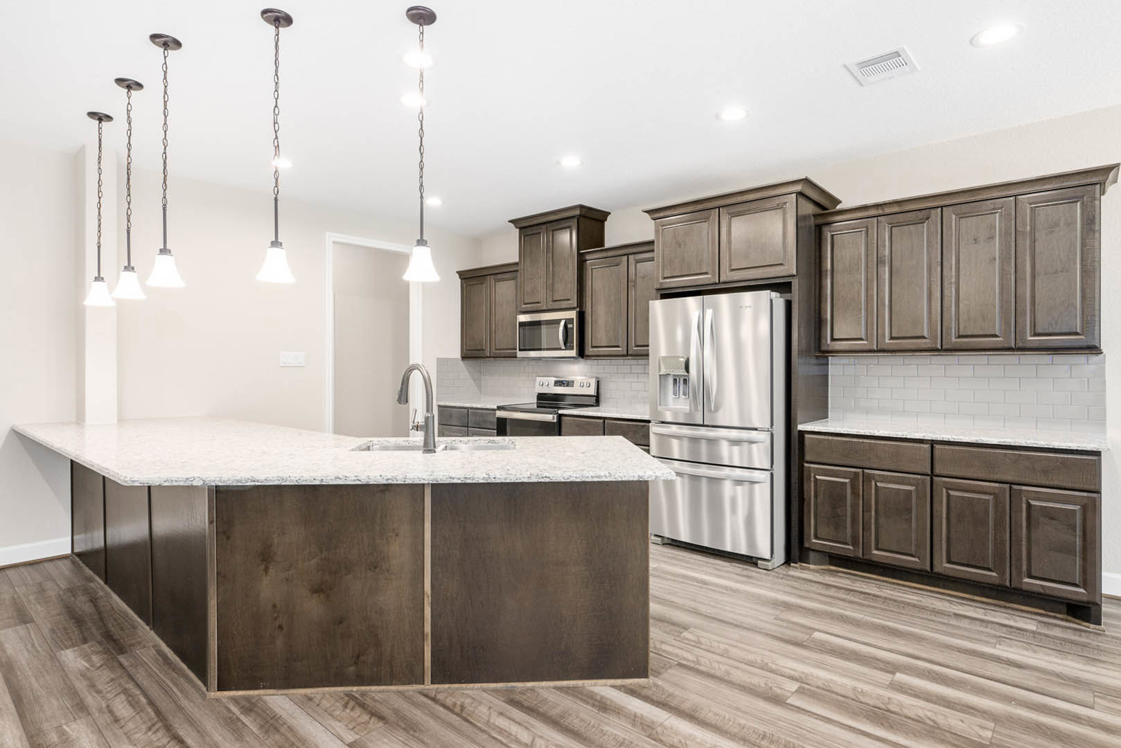 Open kitchen with white cabinetry, quartz countertops, large central island featuring built-in sink, stainless steel refrigerator and microwave, wood flooring, and white vent