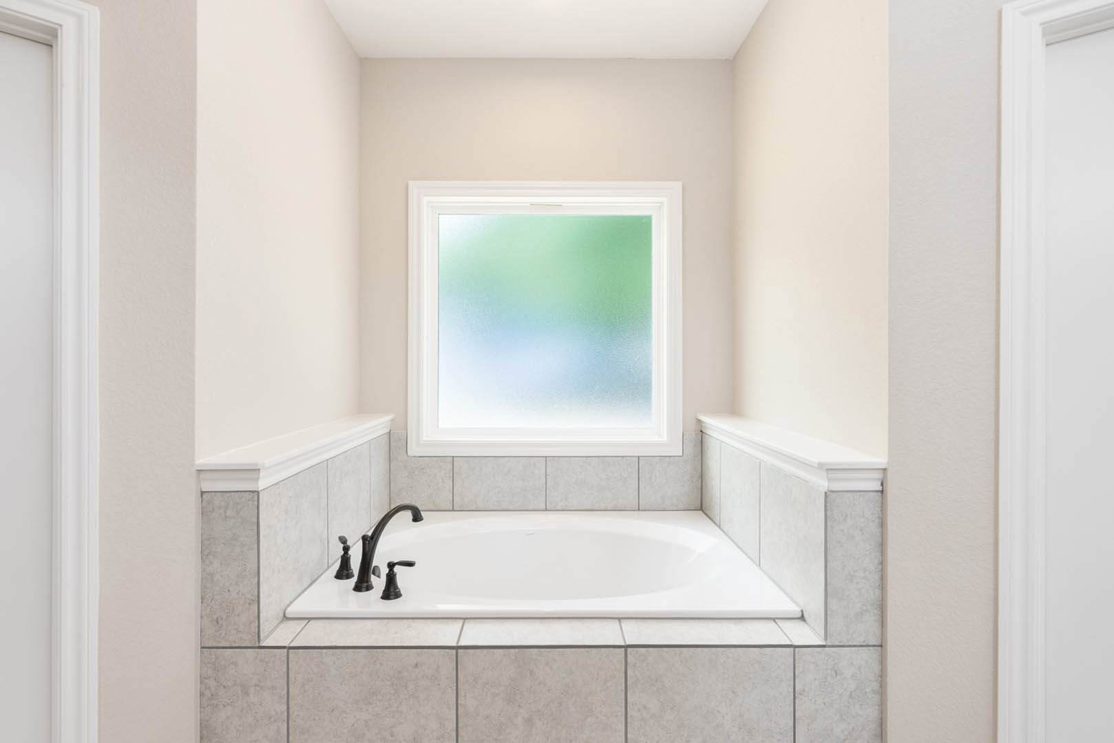 White freestanding bathtub beneath frosted glass window, surrounded by light tile walls and chrome faucet in modern bathroom