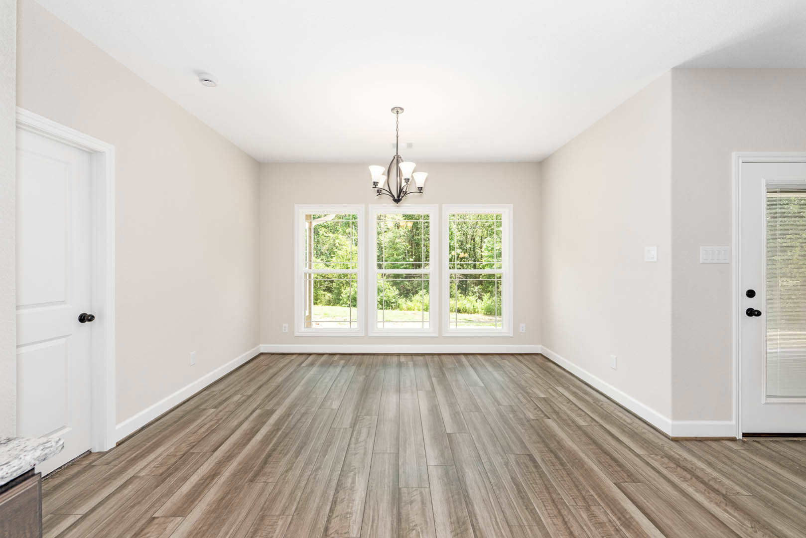Wood flooring with white trim, row of large windows overlooking trees, white door, and chandelier in a bright residential room