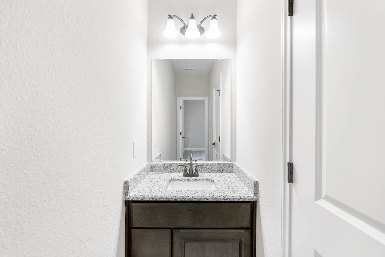 Bathroom with white cabinetry, undermount sink, chrome faucet, large wall mirror, and black hardware on a nearby white door.