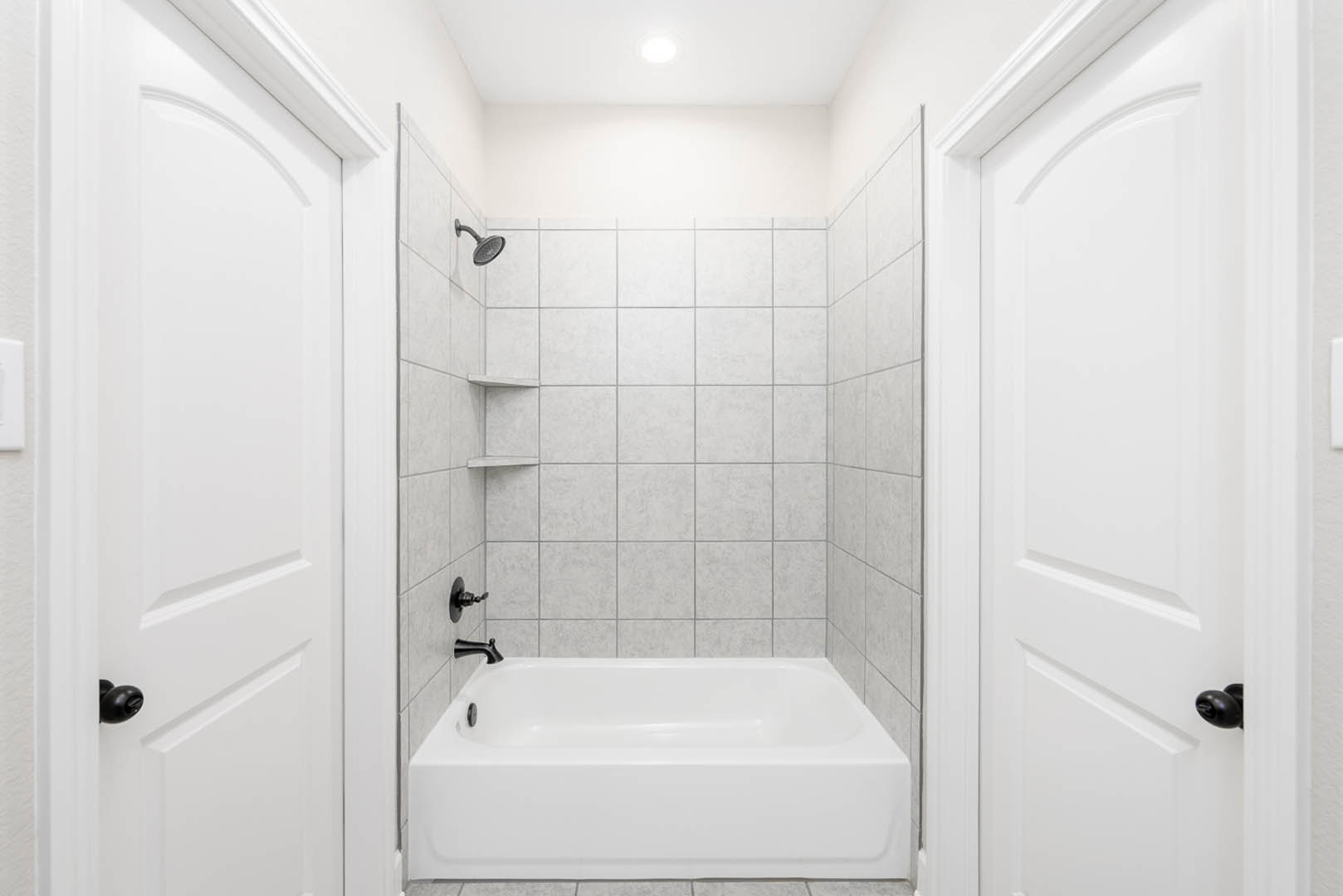 Freestanding white bathtub with chrome faucet, white tile wall and shower head, adjacent white door with silver handle