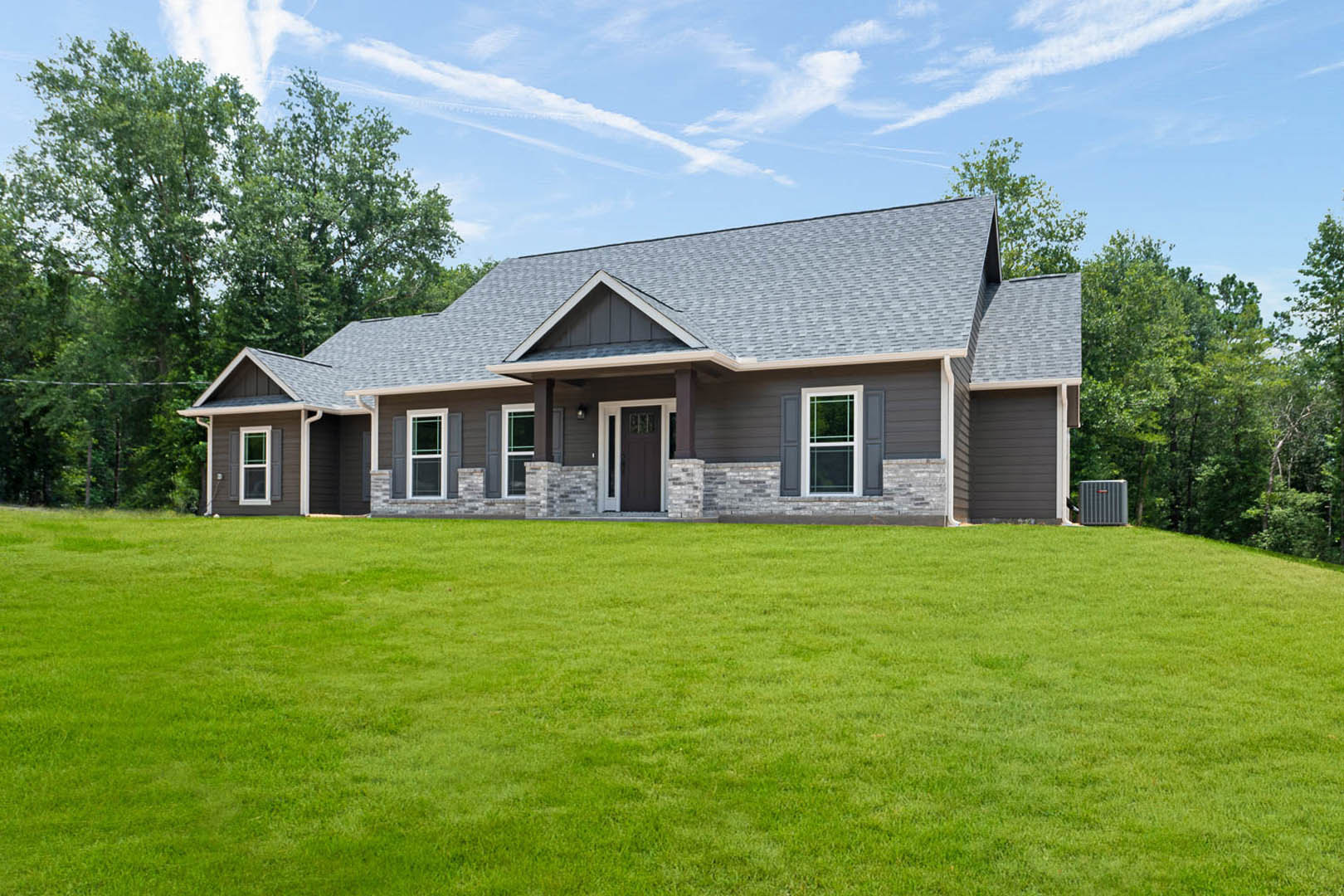 Two-story house with grey roof, white siding, grid windows, and covered porch overlooking manicured green lawn under partly cloudy sky