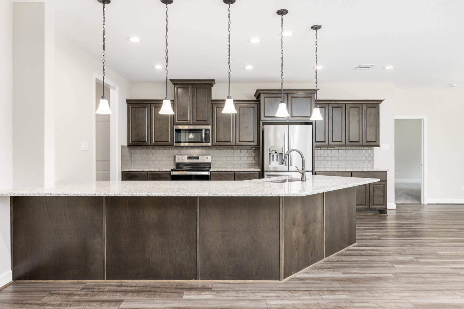 Spacious kitchen featuring a large central island with white quartz countertop, stainless steel appliances including refrigerator, oven, microwave, and black stove, light wood