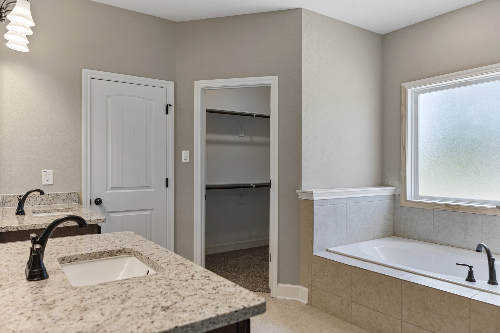 Modern bathroom featuring a freestanding bathtub, white sink with chrome faucet, frosted glass window, tiled walls, and a stone countertop.