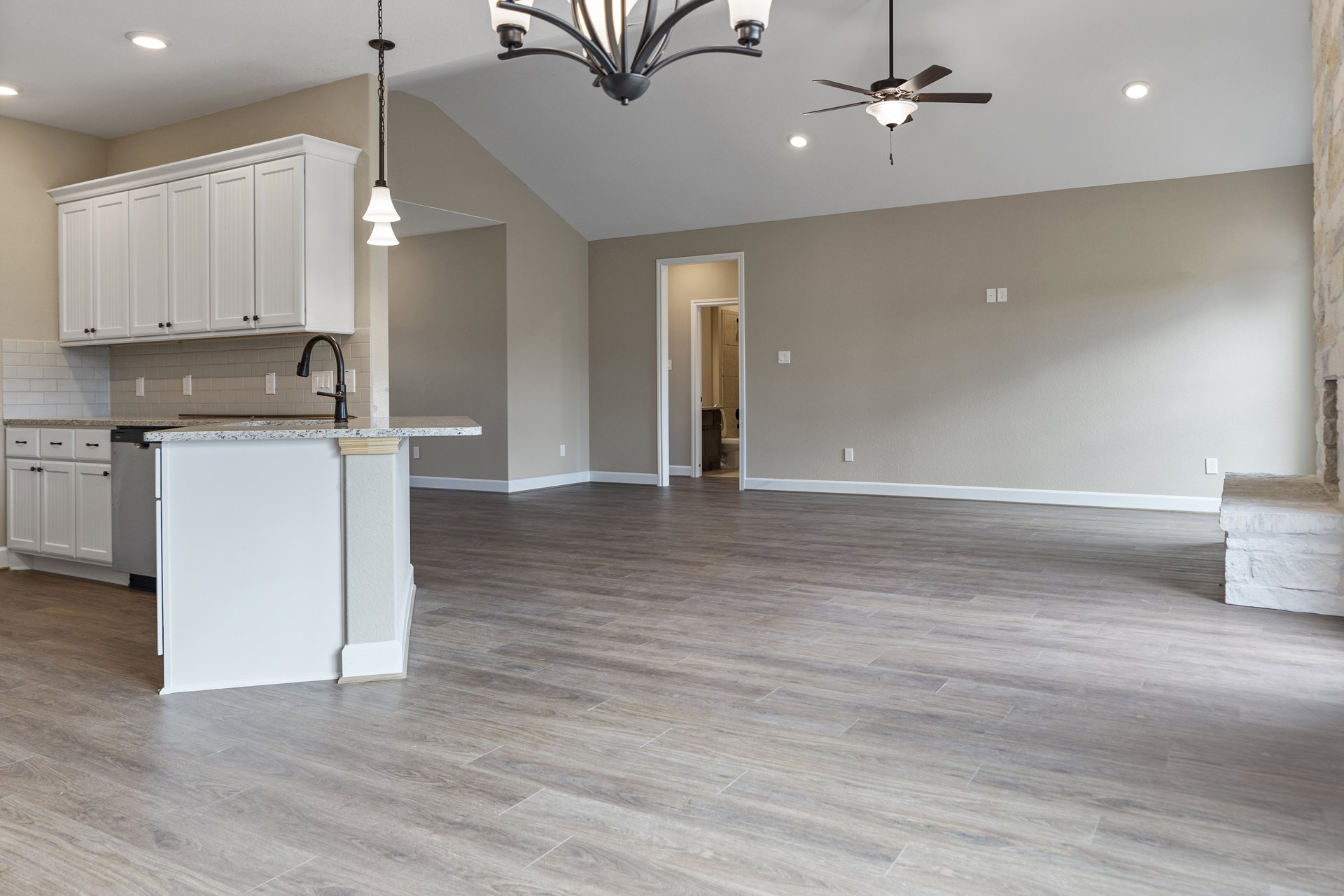 Spacious open floor plan featuring wood flooring, white walls, a kitchen with white cabinets and black knobs, a white island with a black object, dining area, and modern light