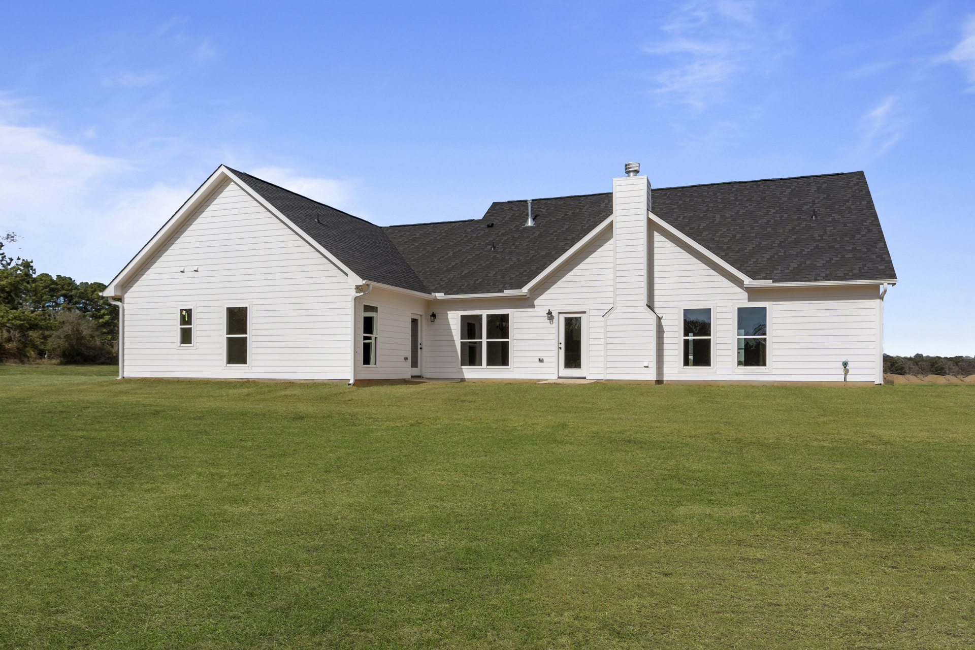 White house with black roof and chimney, surrounded by green lawn, white-framed windows, and Robert Frost Farm visible in the background under a partly cloudy sky.