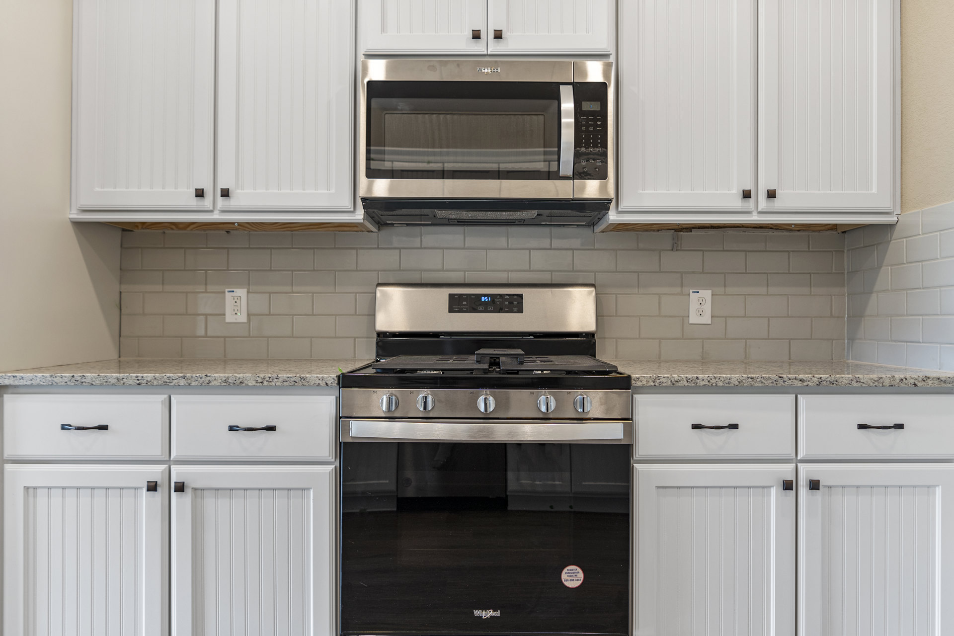 White kitchen cabinets with brown knobs, stainless steel stove with black glass door, open microwave oven above, dark wood flooring