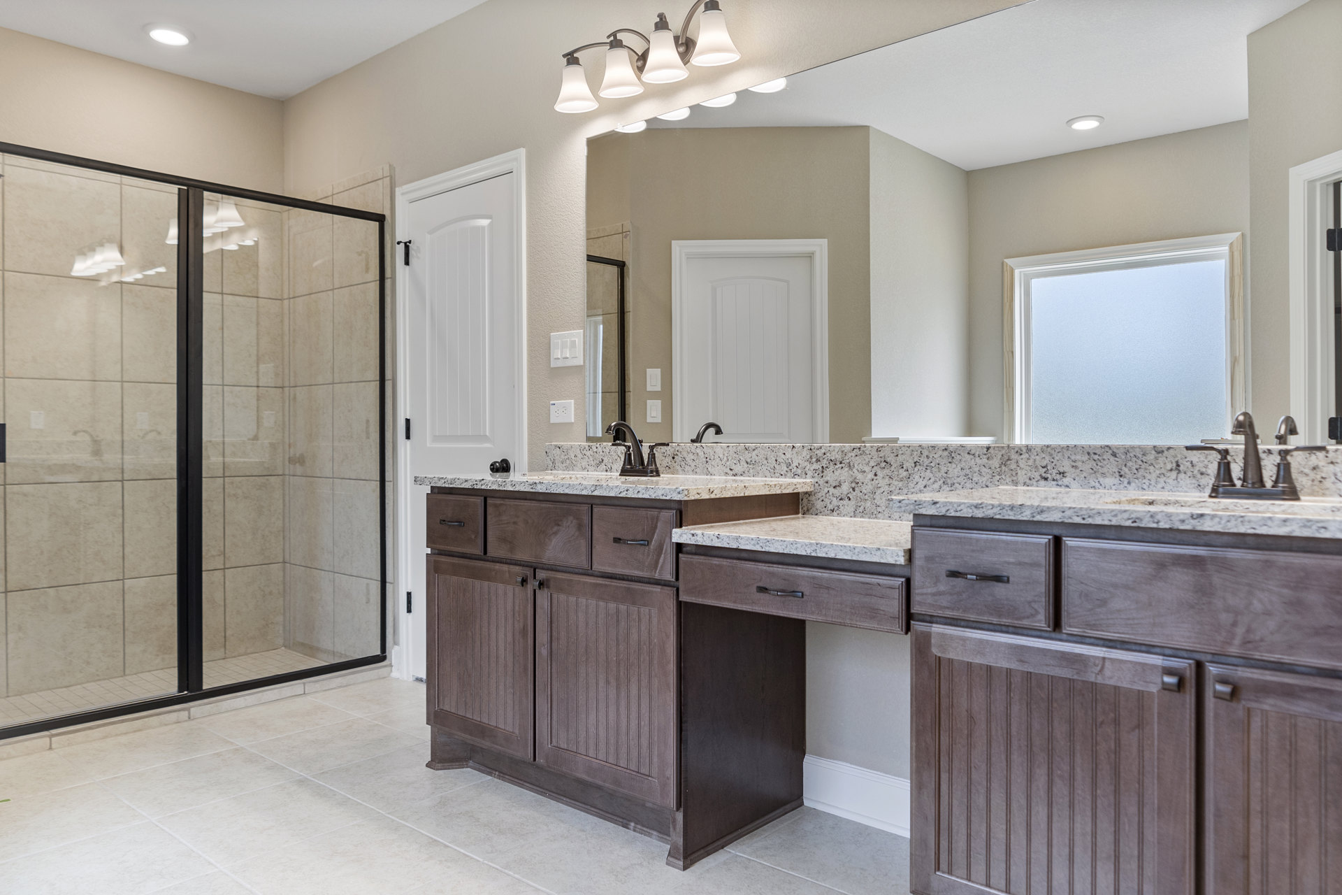 Bathroom featuring a glass-enclosed shower, double vanity with undermount sinks, stone countertop, tile flooring, frosted window, and contemporary light fixture.