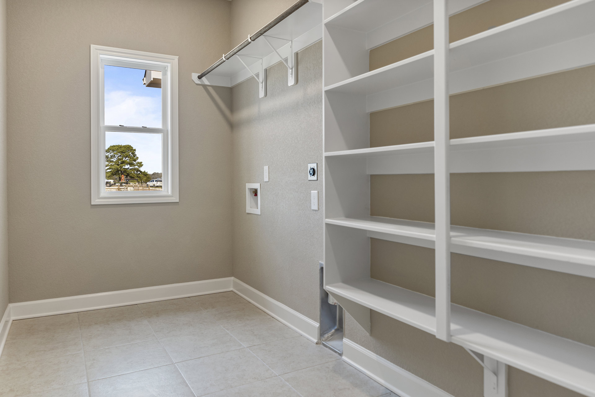 Built-in white shelves on plaster wall, large window with view of tree and trailer outside, white tile floor with matching trim, ceiling with recessed lighting