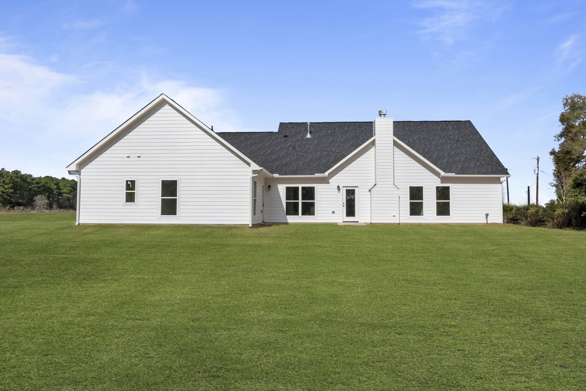 White clapboard house with gabled roof, white-framed windows, and green lawn, Robert Frost Farm visible in background under partly cloudy sky