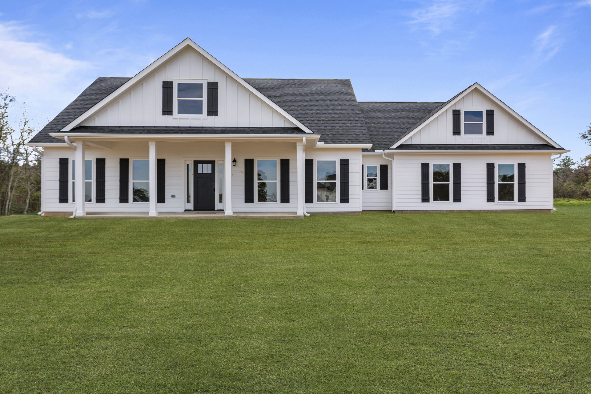 White house with black shutters and a black front door, white-framed windows, covered front porch, green lawn, and partly cloudy sky.