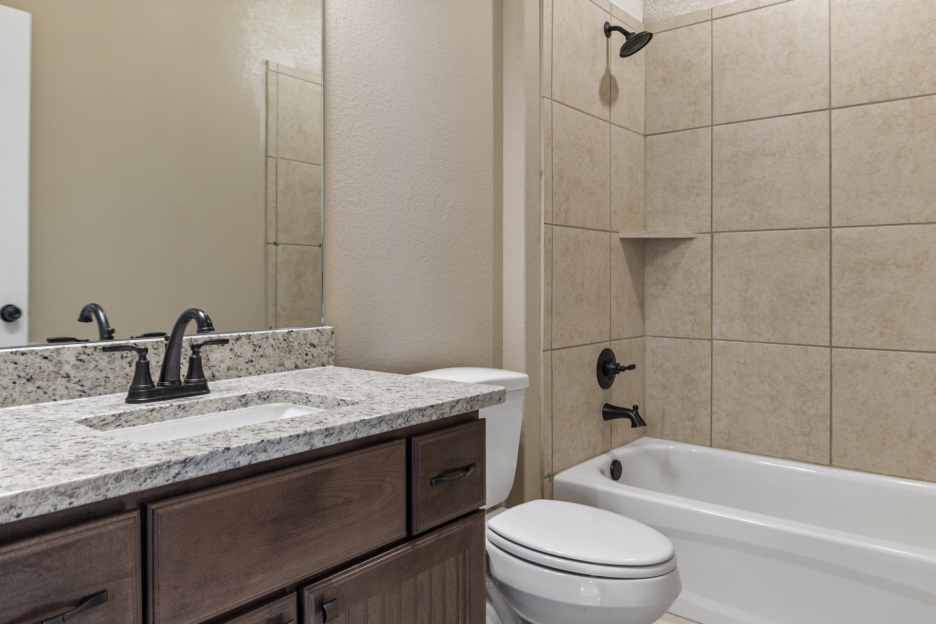 Modern bathroom with white porcelain sink and toilet, chrome faucet, tiled shower wall, and neutral tile flooring