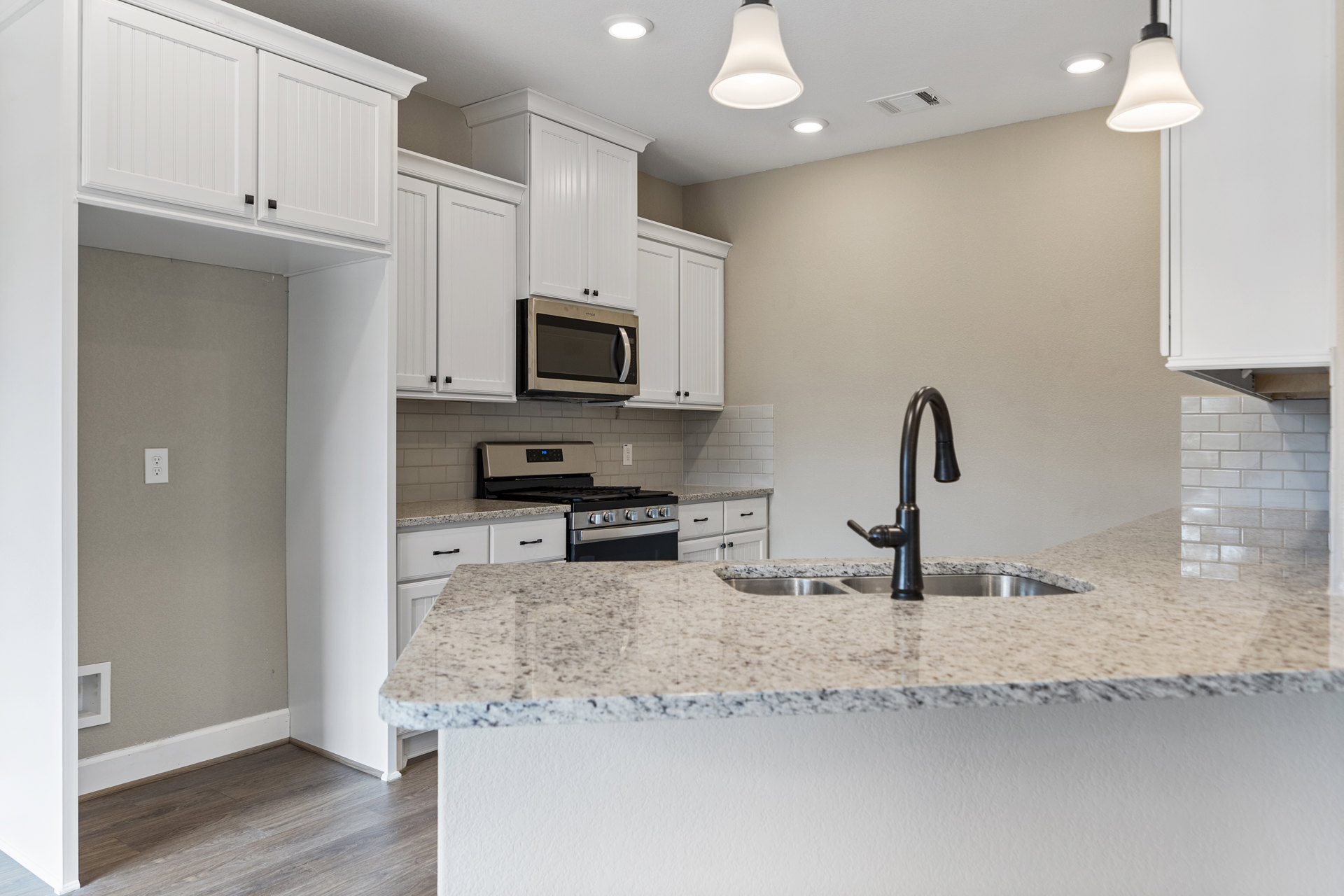 White cabinetry and countertops with a black faucet and stainless steel sink, built-in microwave above, white ceiling lamp shade, light wood flooring