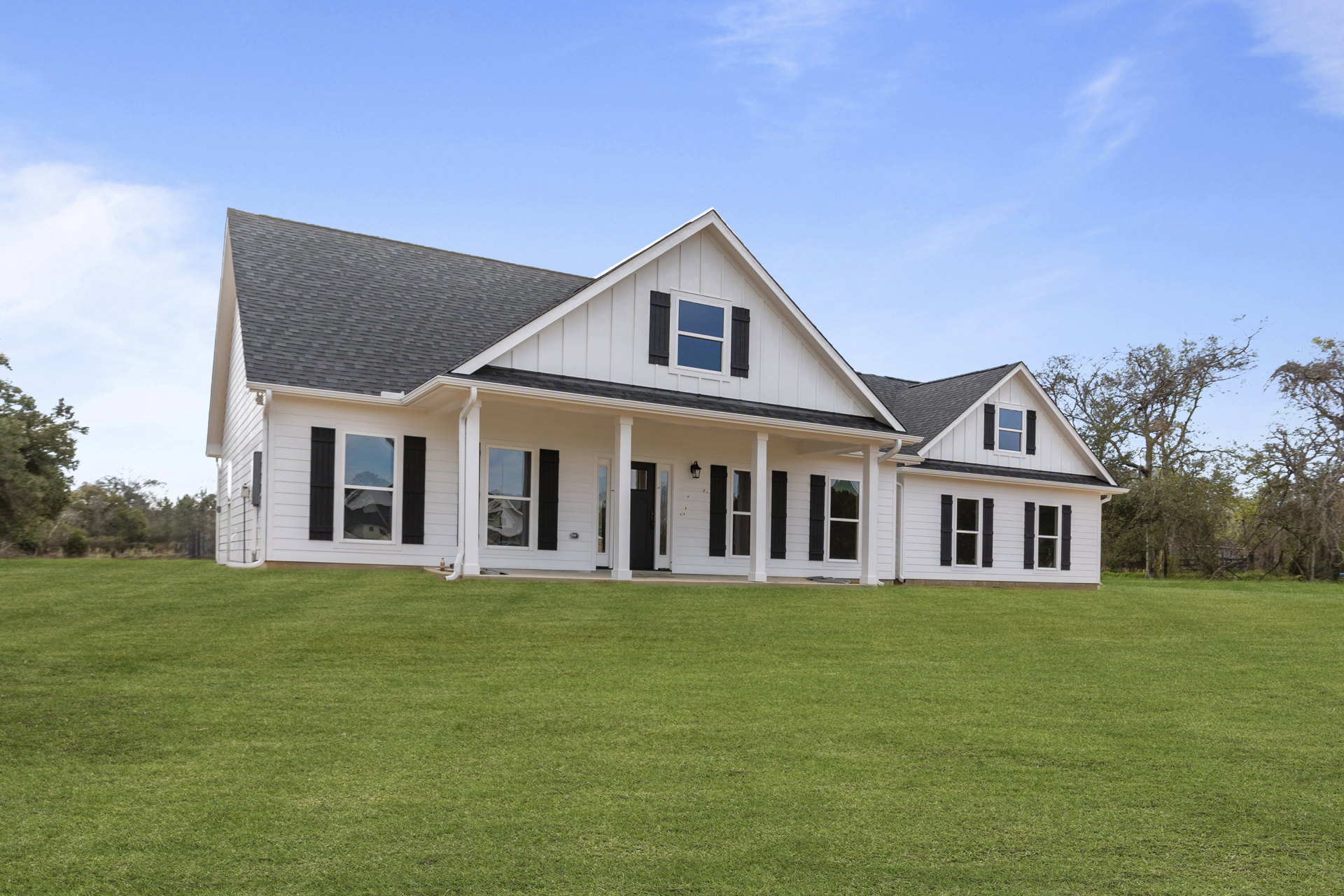 Large white house with black shutters, prominent columns on the front porch, expansive green lawn, blue sky with scattered clouds