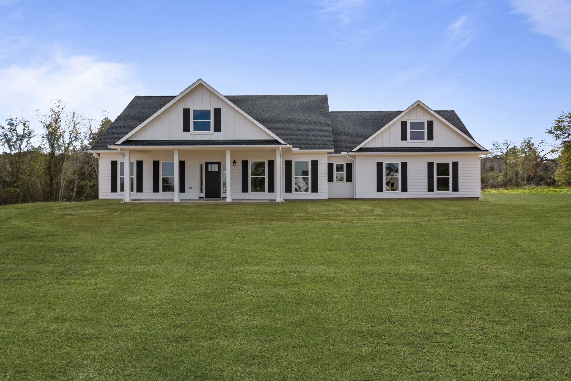 White two-story house with black shutters and black front door, expansive green lawn, covered porch, windows, cloudy sky, bird flying overhead