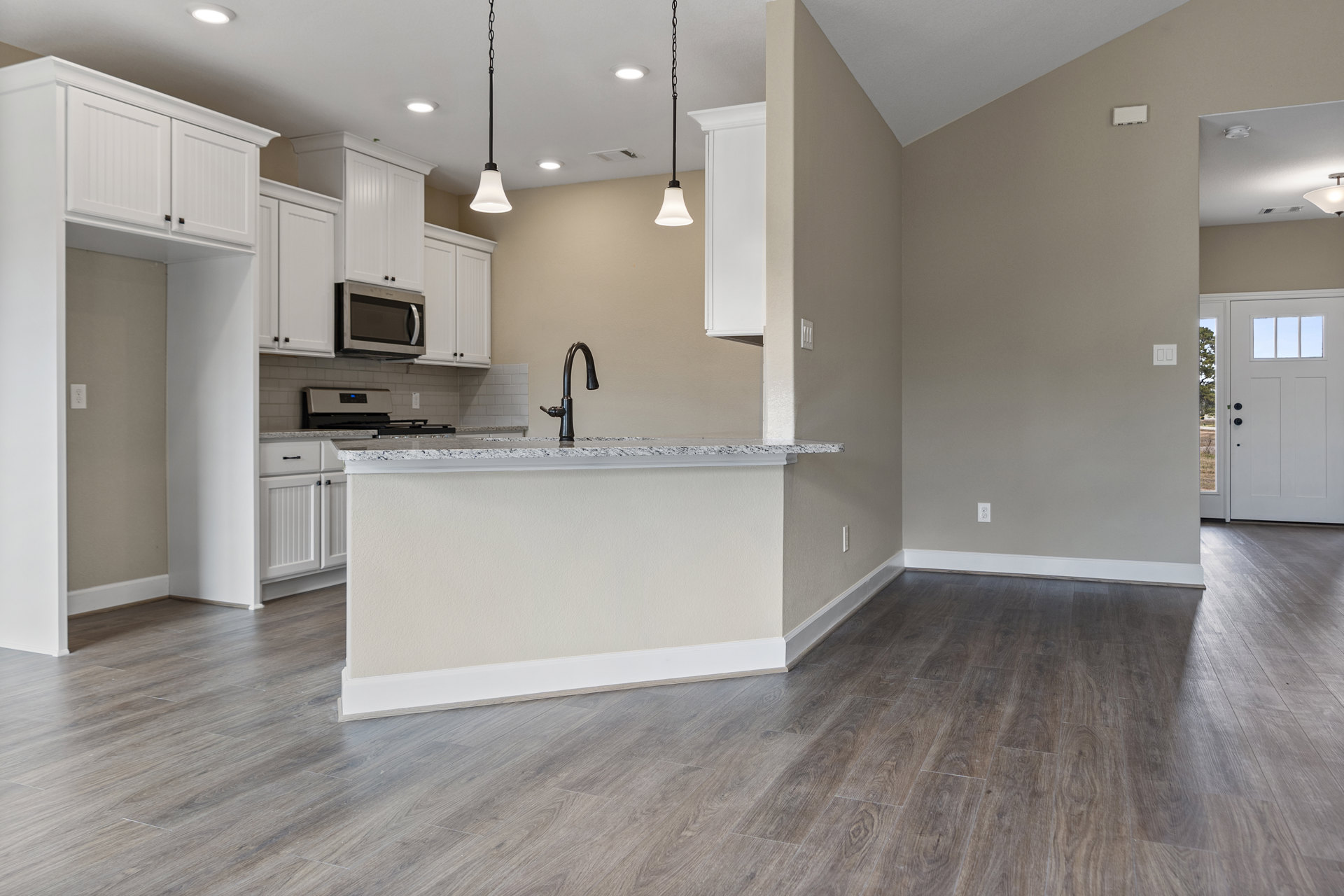 Kitchen with wood flooring, wood cabinetry, black curved faucet at a sink set in a light countertop, microwave oven with door, white door with window, wood wall accents