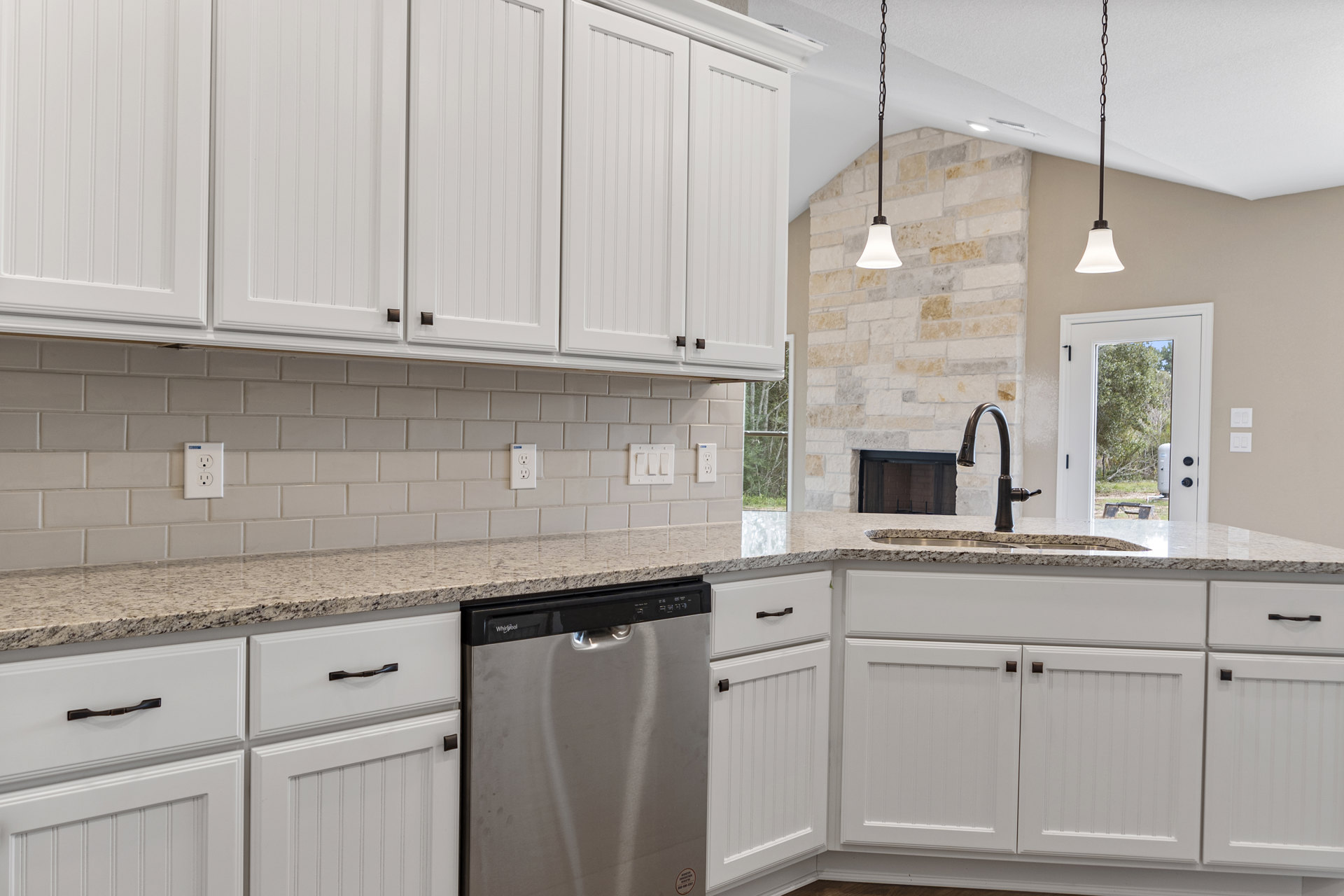 White kitchen cabinets with granite countertops, stainless steel sink, black-handled dishwasher, glass window door, electrical outlet, and modern light fixture