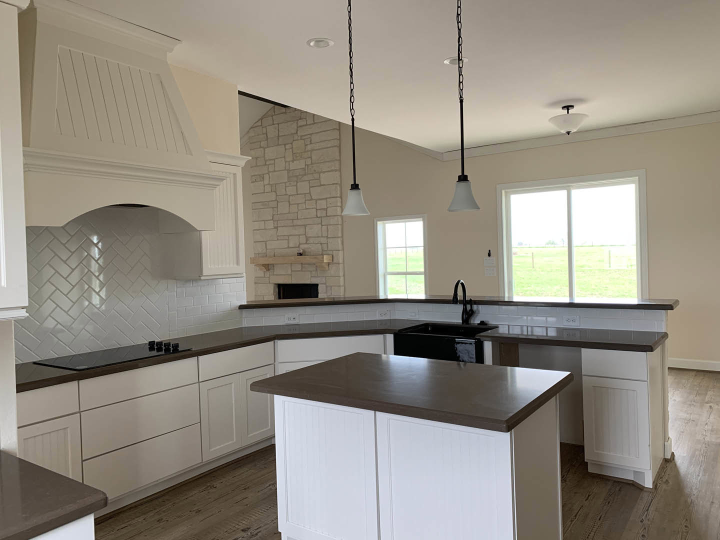 White kitchen with black countertops, white cabinetry, black sink, tile backsplash, window overlooking green grass field