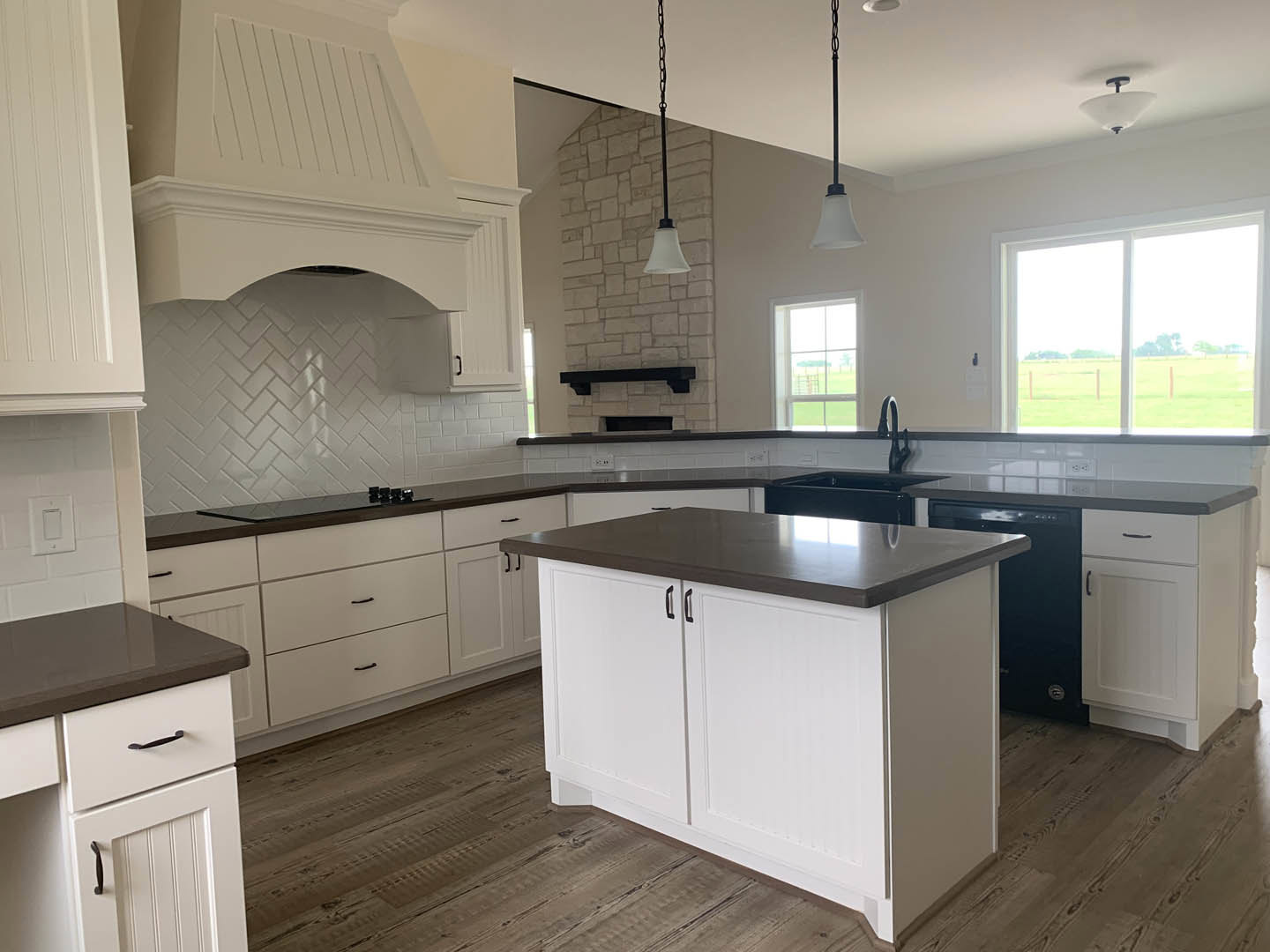 White kitchen with black countertops, white cabinetry, dark kitchen island, tile flooring, stainless steel sink, window overlooking a field, close-up of drawer, white light fixture