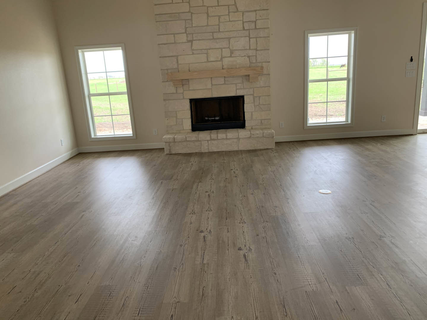 Living room with hardwood floors, white walls, black-framed rectangular fireplace, and large windows overlooking grassy field.